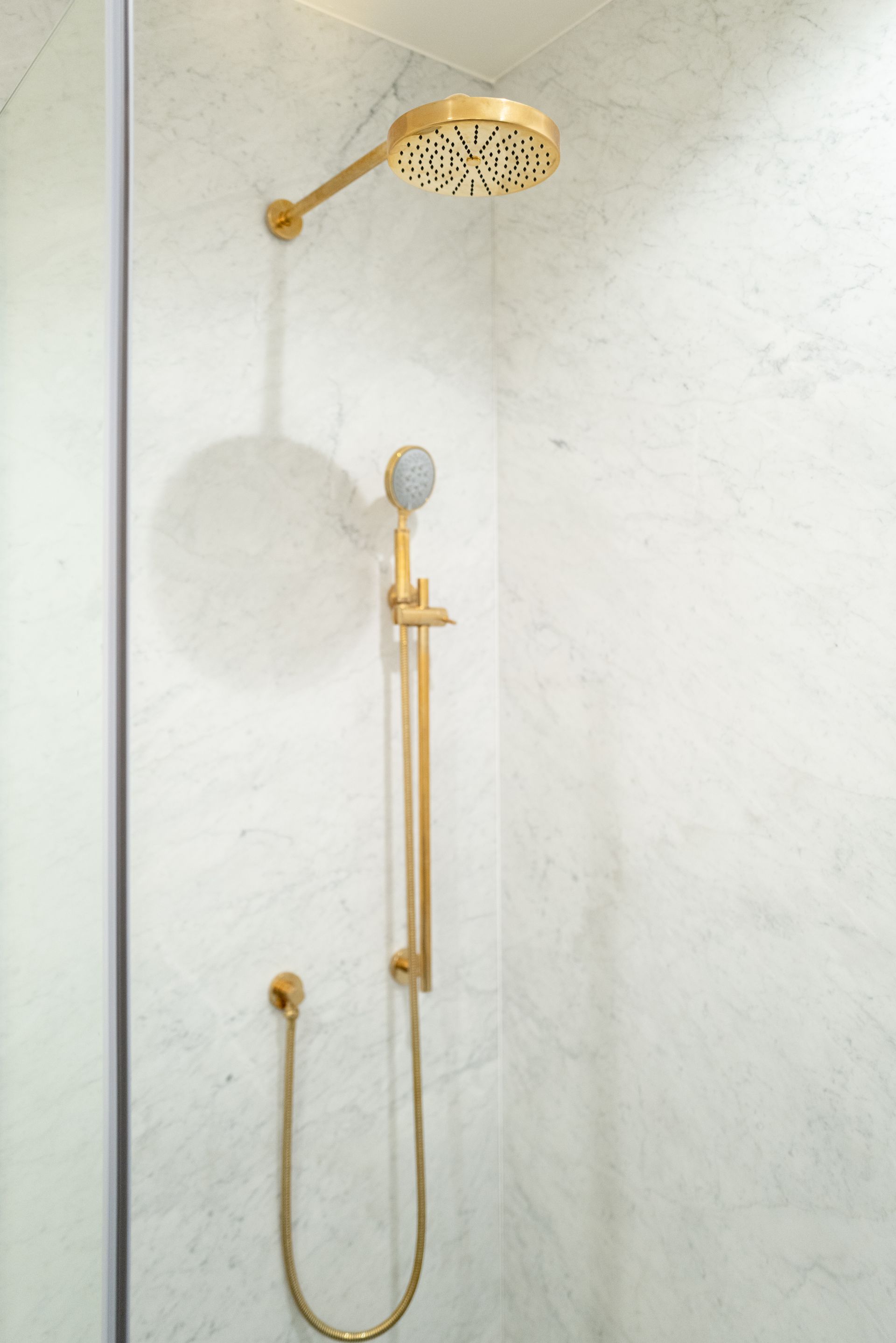 Gold showerhead and hand shower with hose mounted on white marble bathroom wall