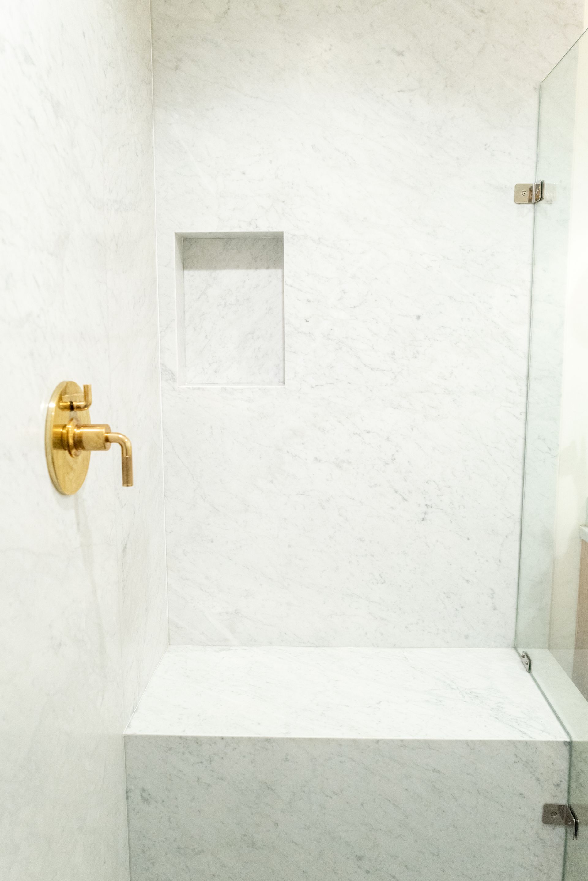 White walk-in shower with gold faucet, small recessed shelf, and built-in bench.