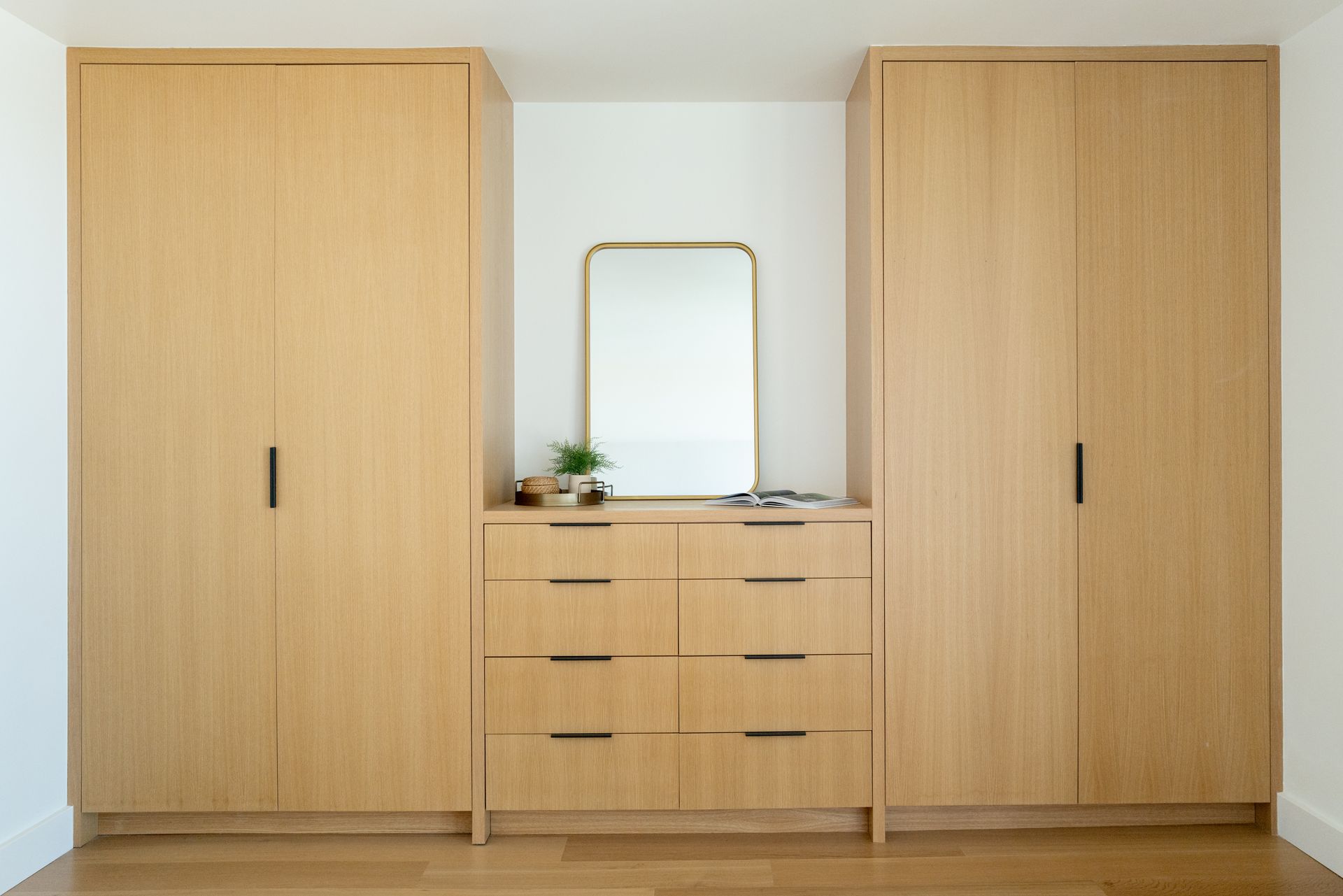 Two light wood wardrobes flanking a matching dresser with a mirror in a bright bedroom
