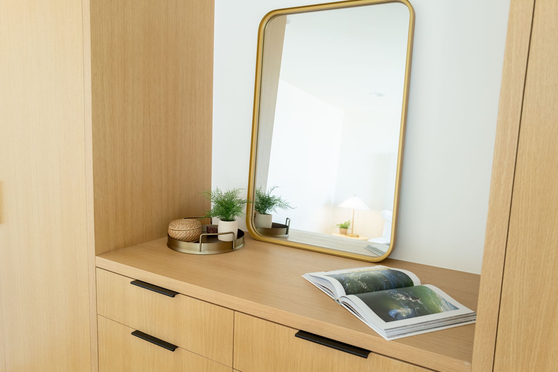 Wooden dresser with gold-framed mirror, small decor, and an open book in a light-colored room