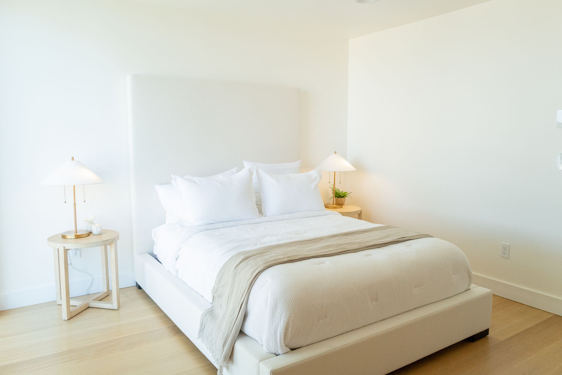 Bright minimalist bedroom with white bed, bedside lamps, and light wood floor