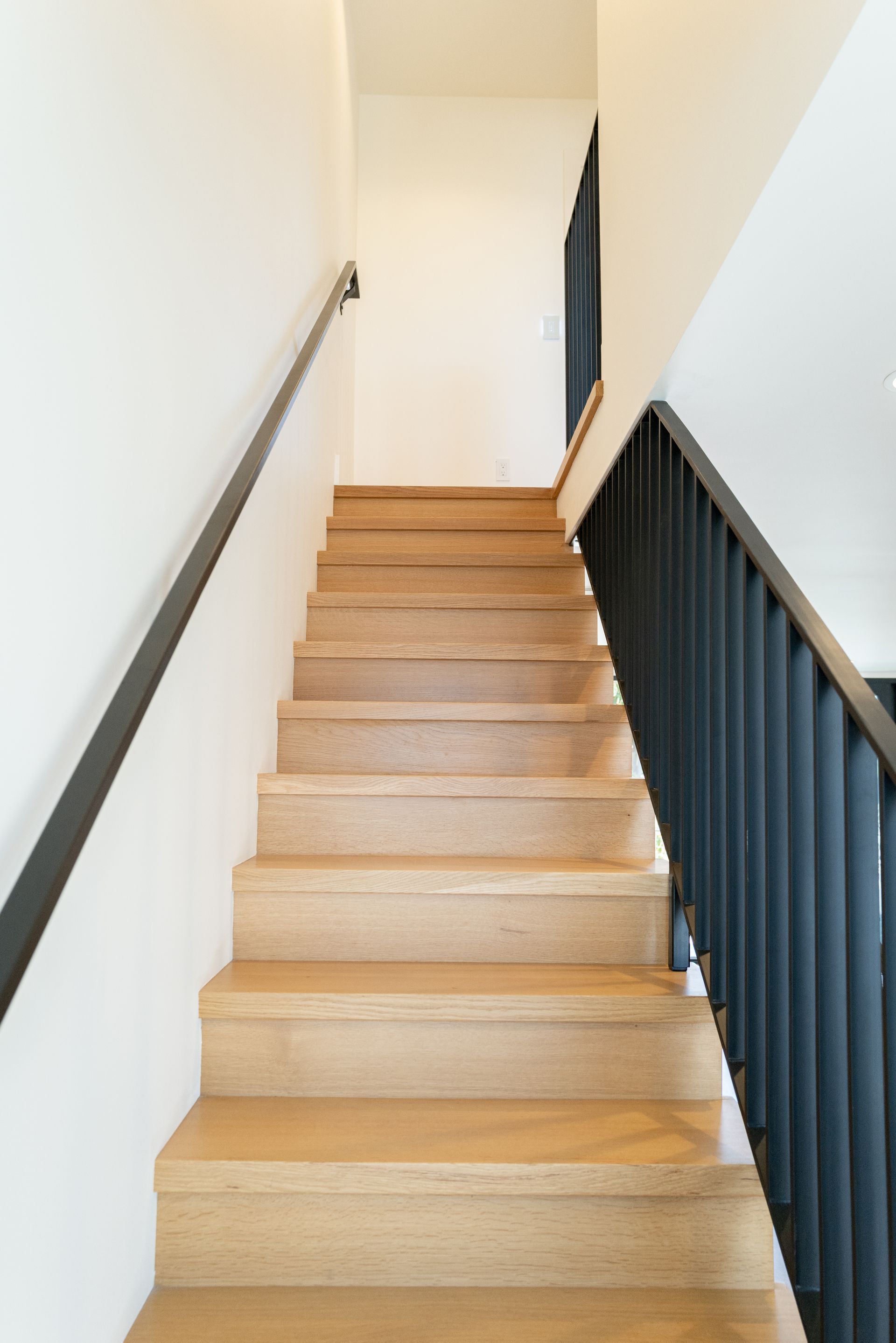 Wooden staircase with black railing leading up to a bright white landing.