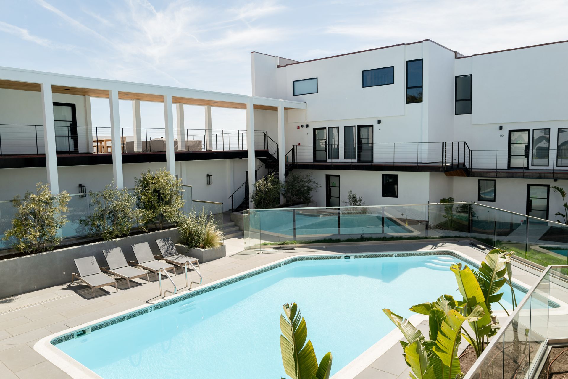 Modern apartment courtyard with a swimming pool, lounge chairs, and white buildings under a clear sky