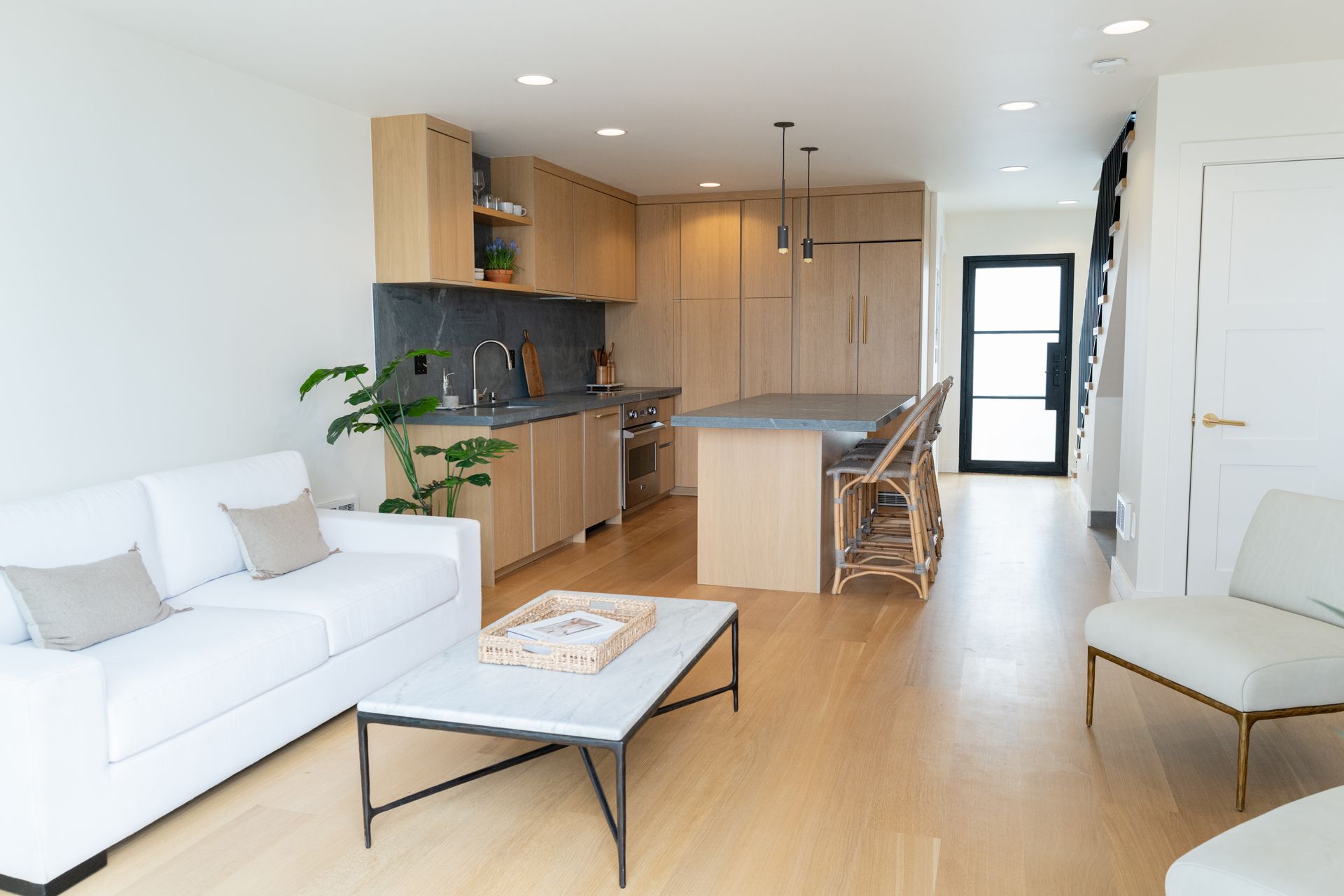 Bright modern open-plan living room and kitchen with white sofa, wooden cabinetry, and dining island