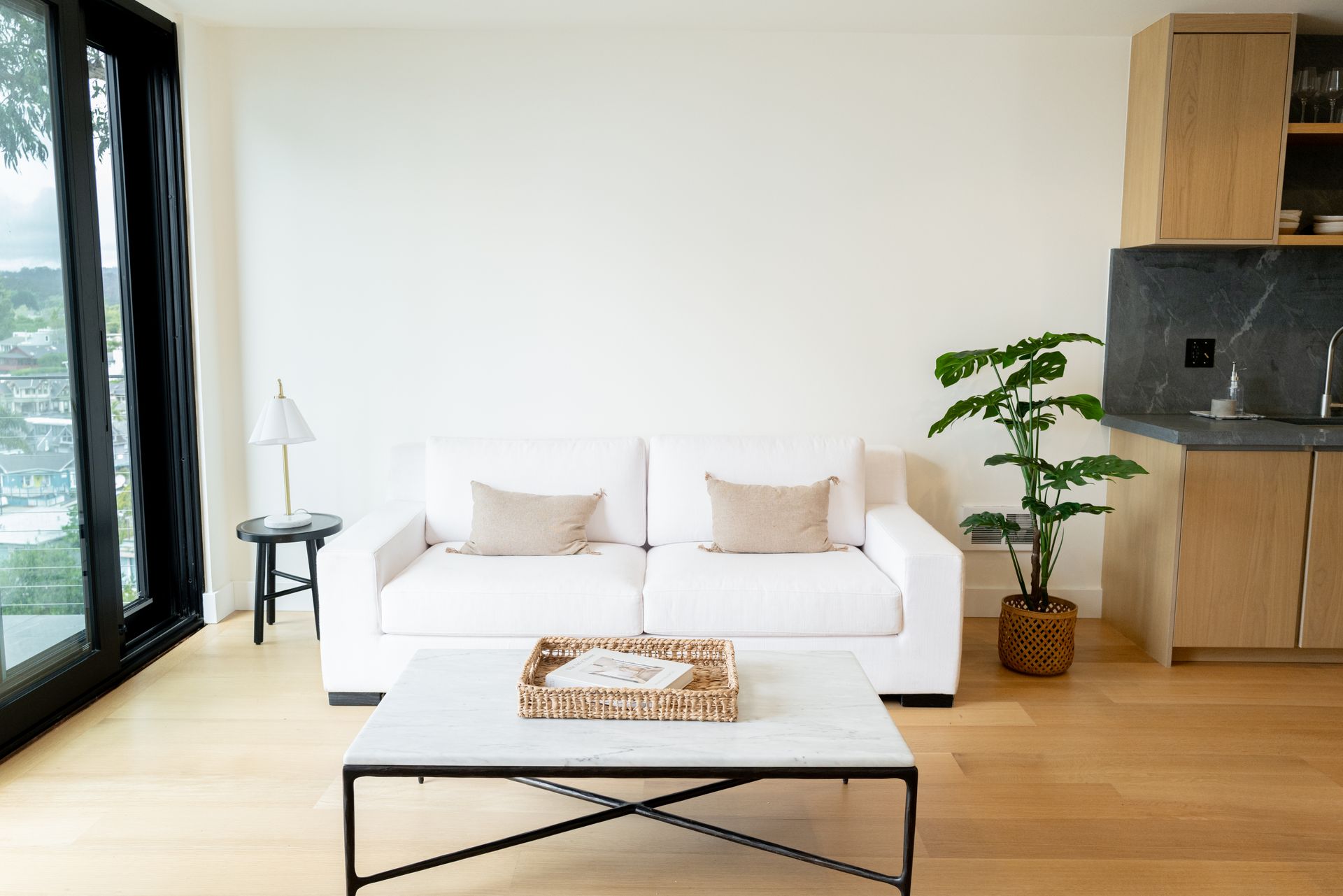 Bright living room with white sofa, coffee table, potted plant, and large windows.