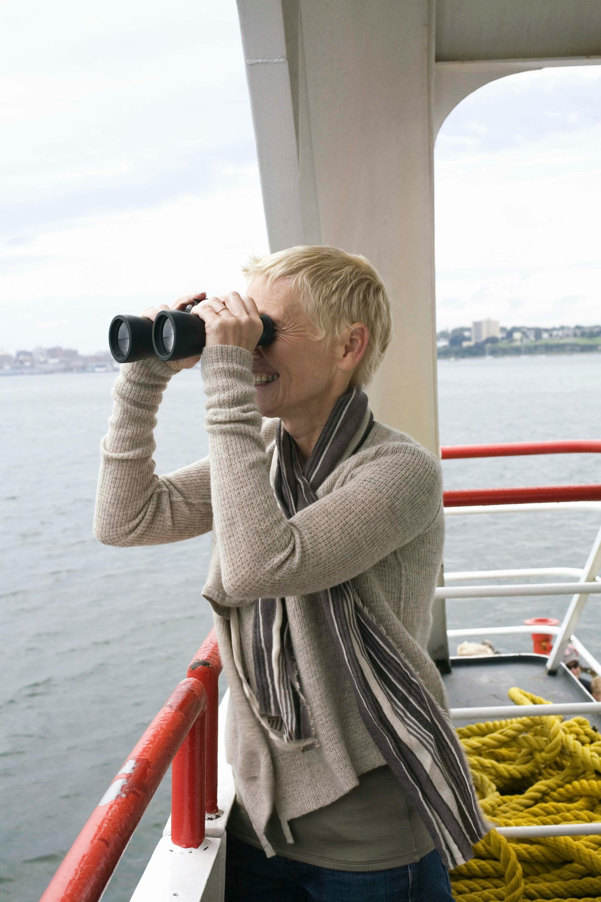 Person using binoculars on a boat deck, with red railing and water in the background