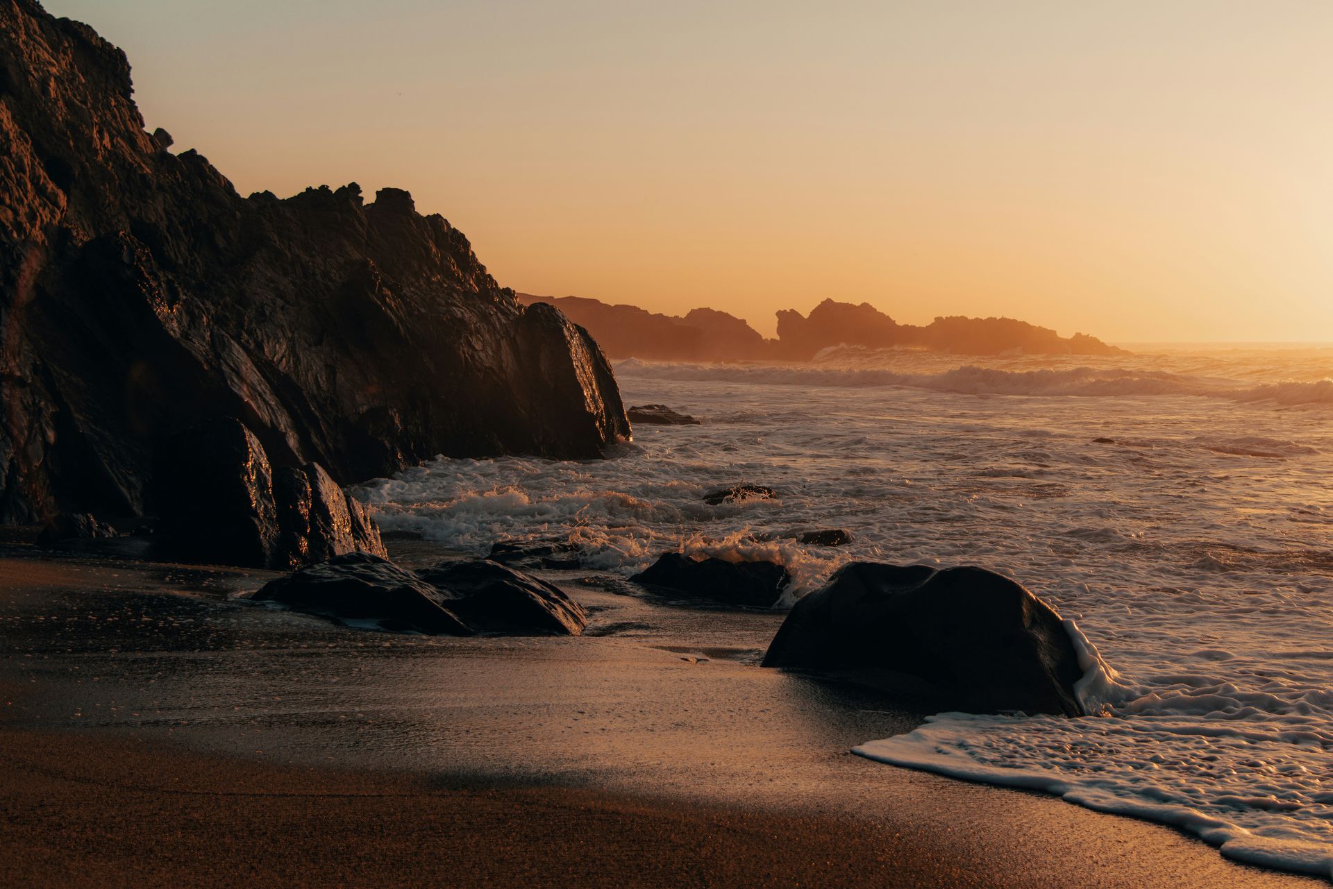 Rocky beach at sunset with waves washing over the shore and orange light on the water