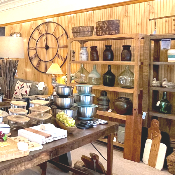 Wooden shelves display kitchenware and decor in a shop, including clocks, bowls, and glass bottles.