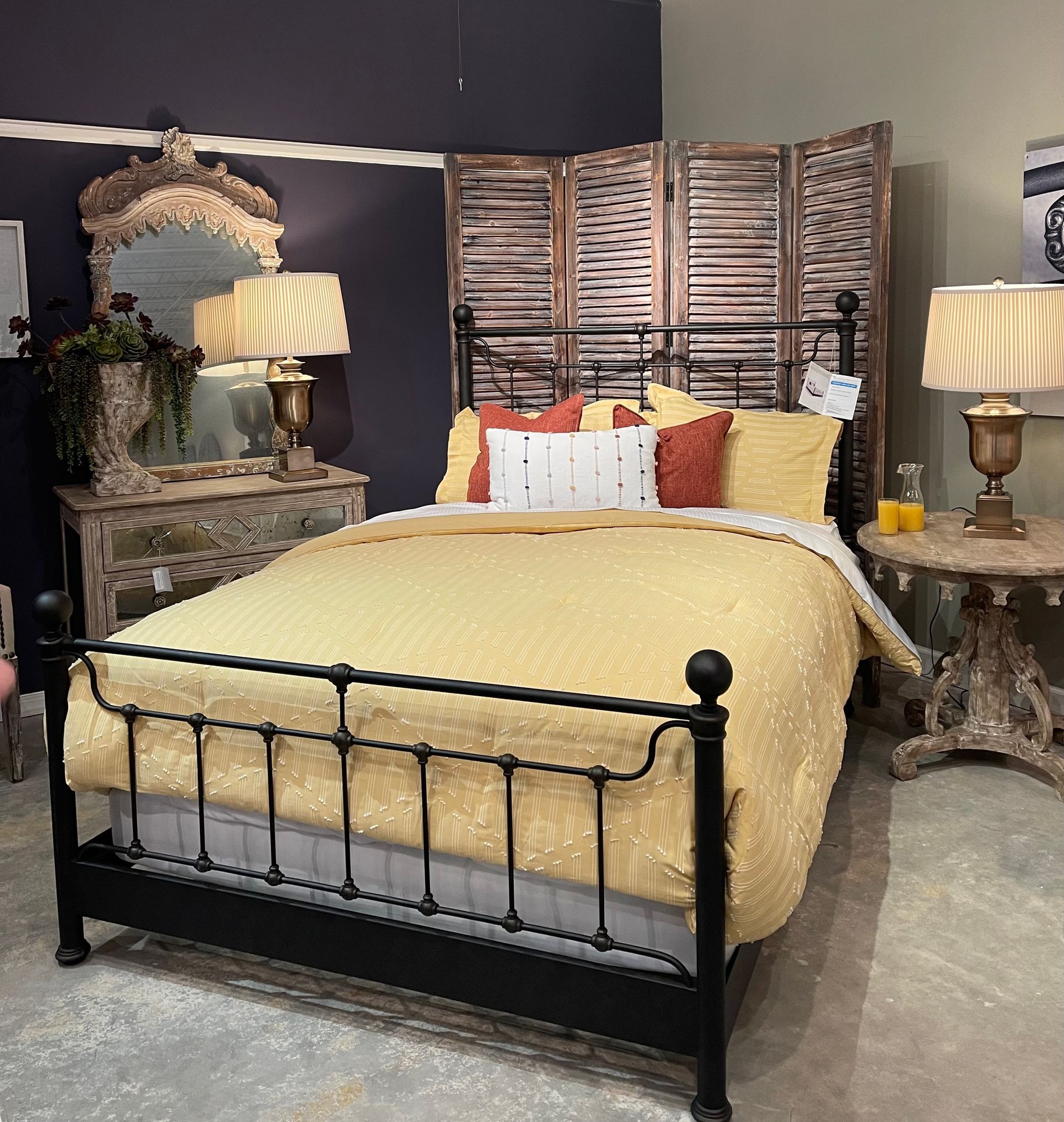 Black metal bed with yellow bedding in a room with antique furniture.