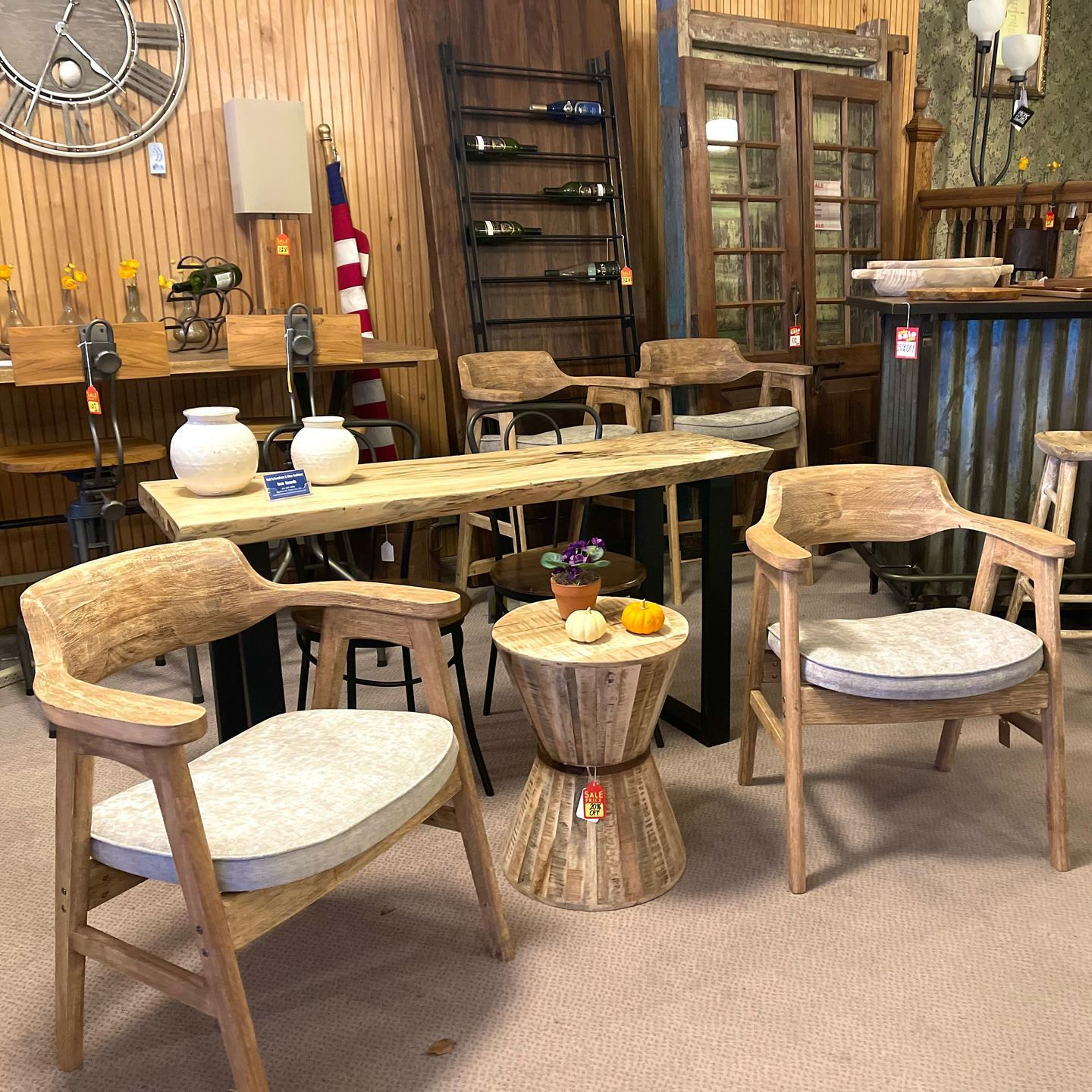 A furniture store interior featuring wooden chairs, a table, a small side table, and a metal wine rack.