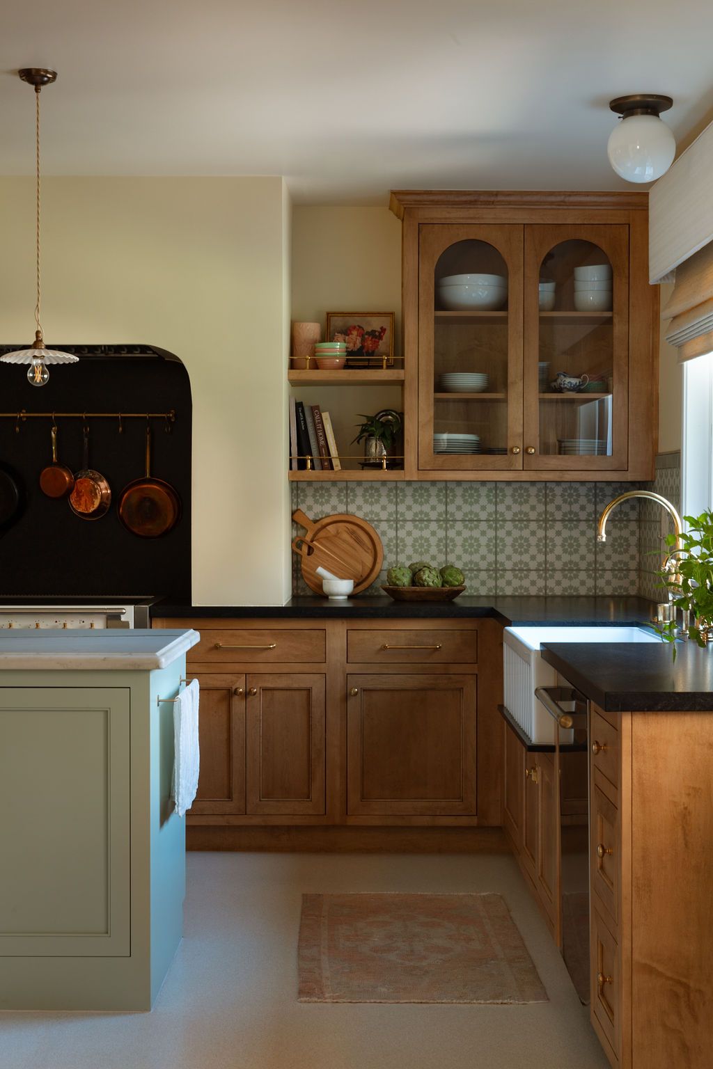 A kitchen with light green island cabinets, natural wood cabinetry, patterned tile backsplash, and a white farmhouse sink.