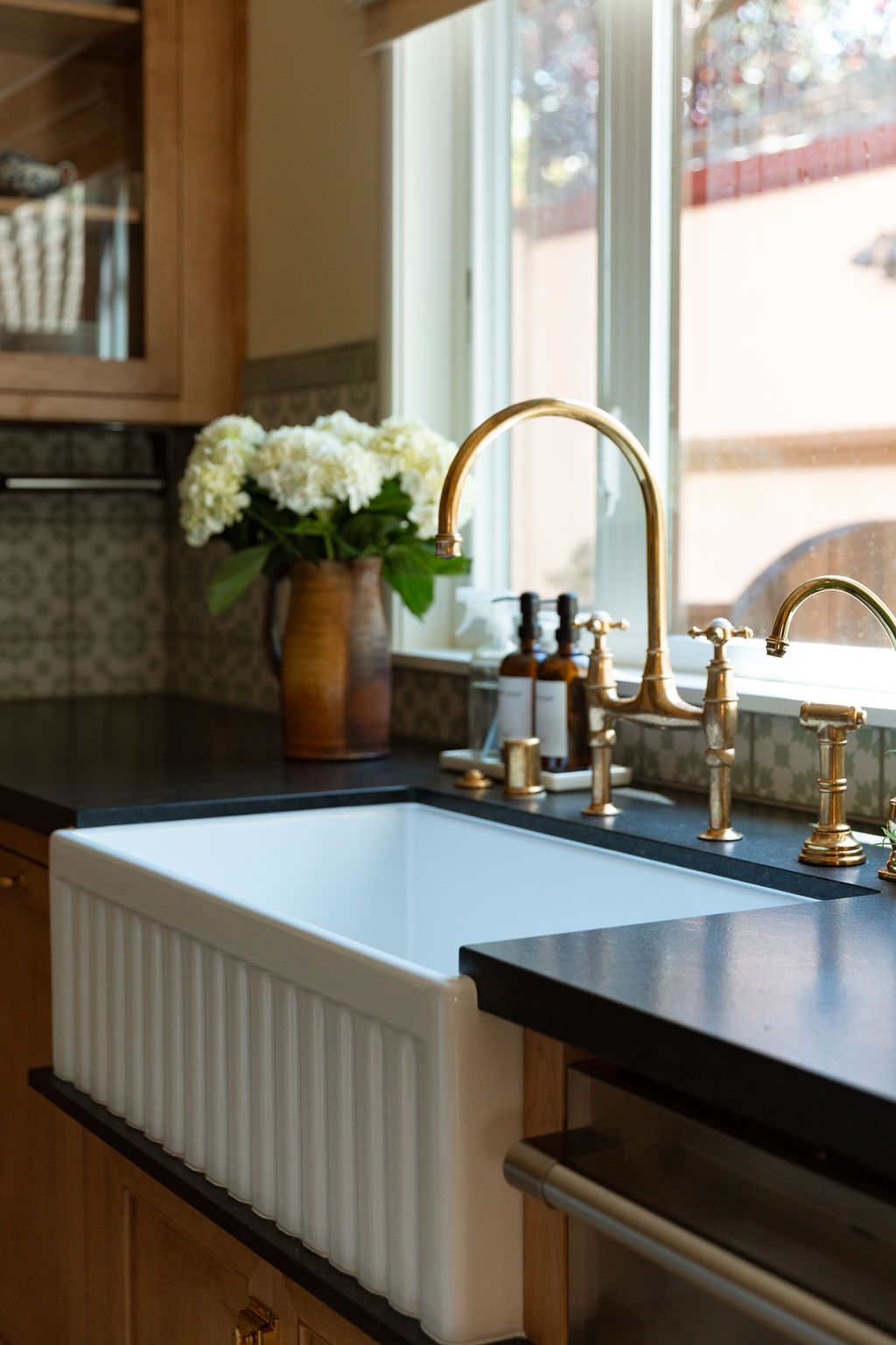 Bathroom remodel with a white farmhouse sink, black countertop, and gold faucet. 