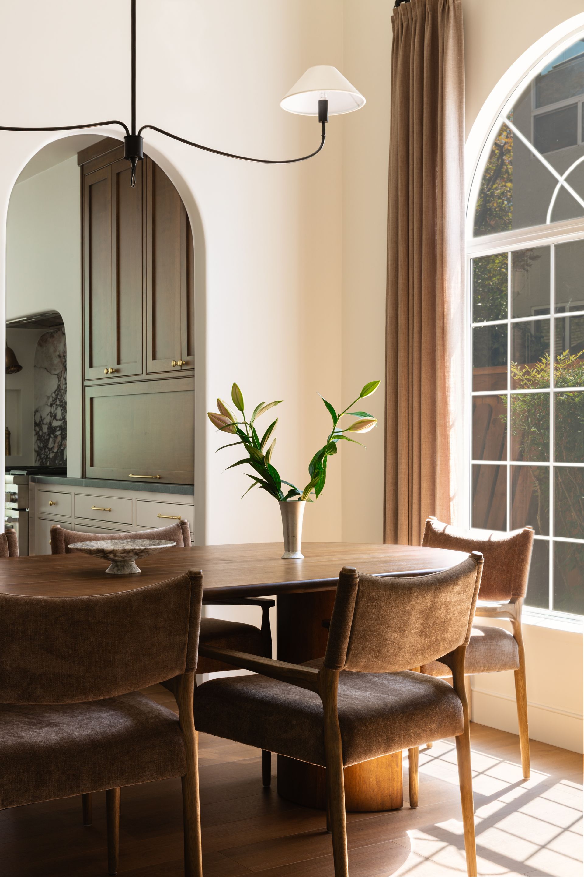 Custom home remodel detail with a minimalist black chandelier, elegant drapes, and an arched window.