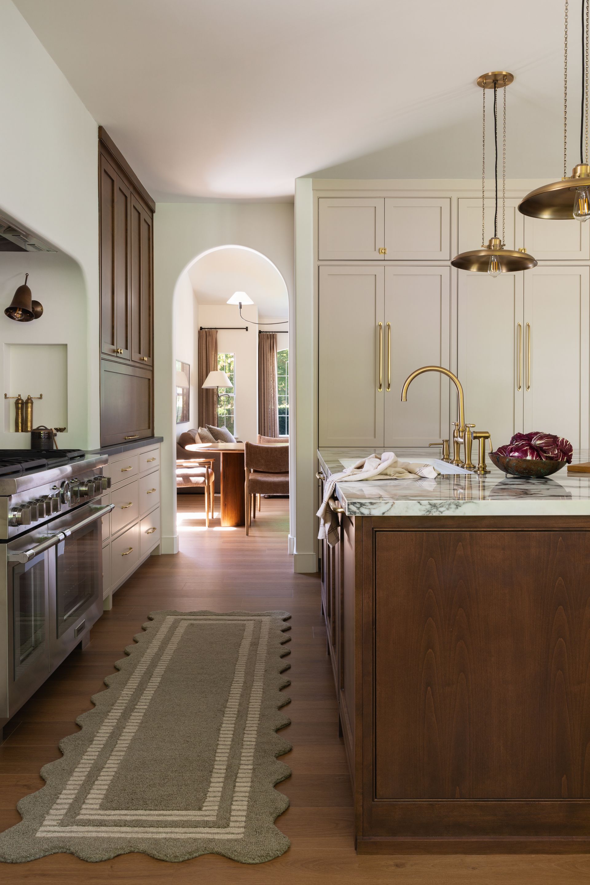Custom home remodel kitchen detail showing cream cabinetry with brass hardware, pendant lights, and an arched doorway.