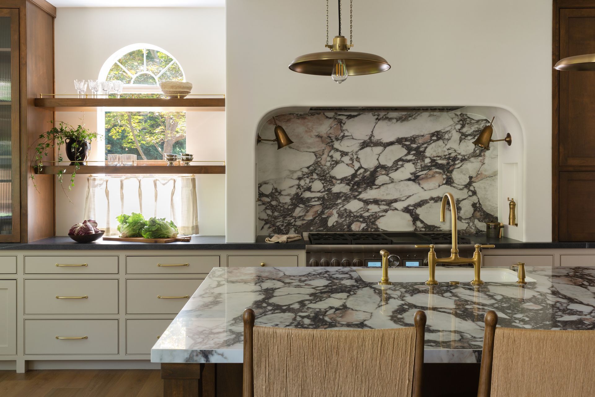 A modern kitchen featuring light cabinets, a large marble island, a matching marble stove backsplash, and arched shelving.