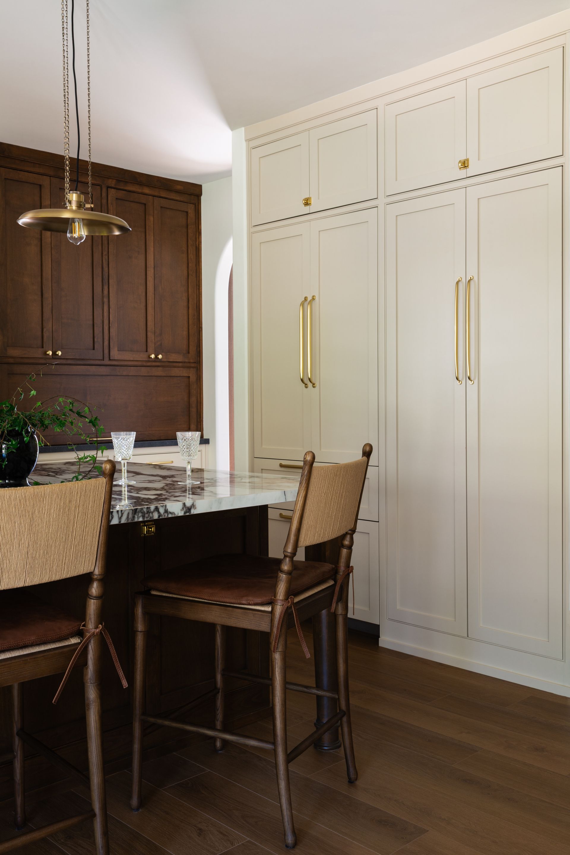 Luxury kitchen remodel with cane-back stools, a marble island, dark wood cabinetry, and a brass pendant.