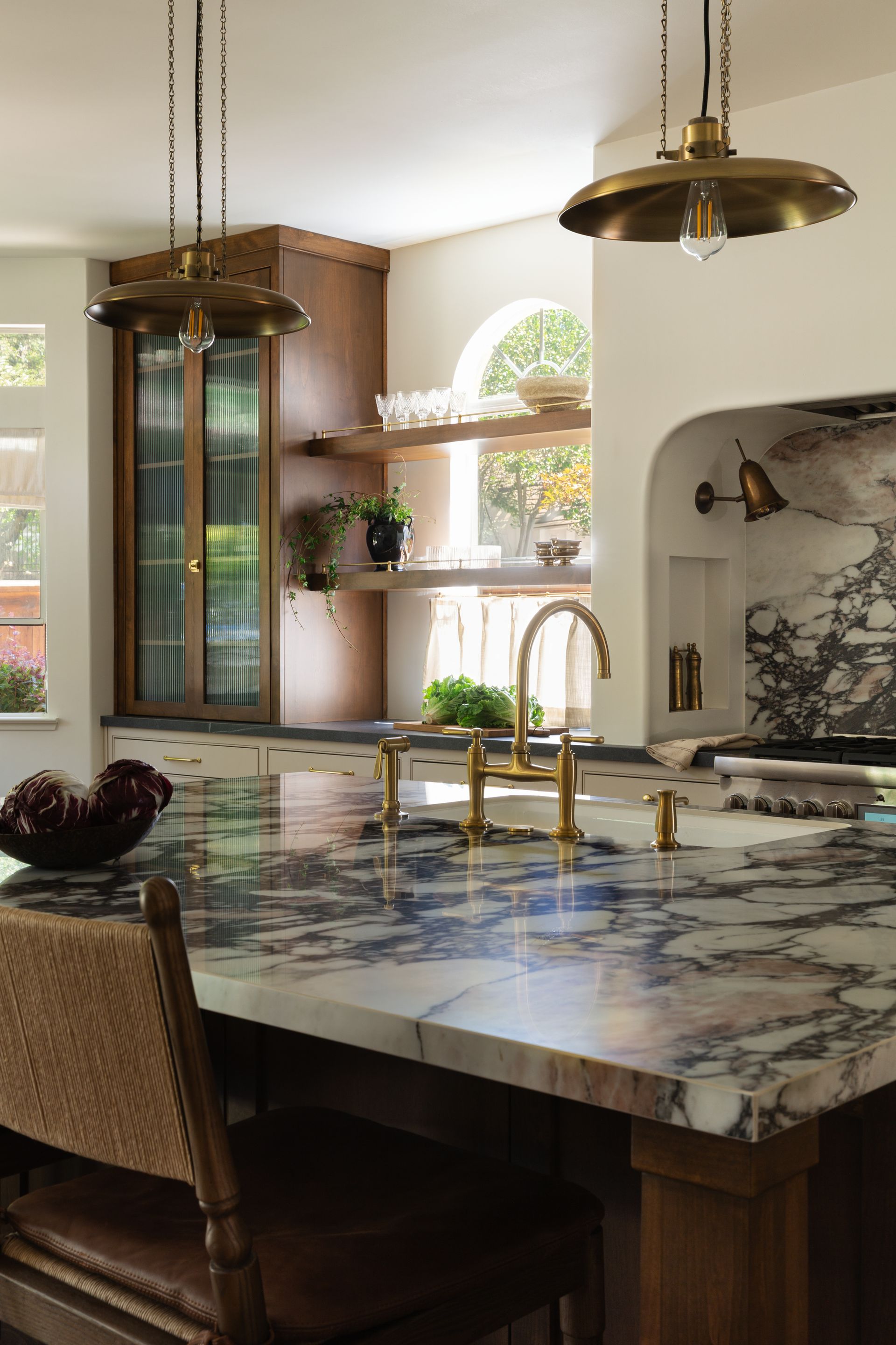 Luxury kitchen remodel detail showing two brass pendant lights, dark wood cabinets, and an arched window.