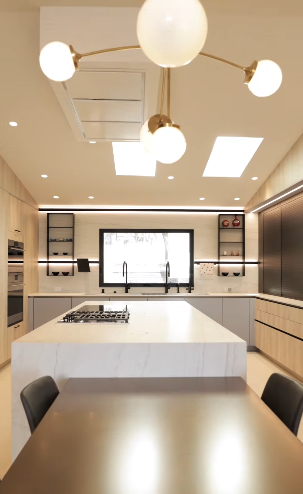 Luxury kitchen remodel with white island, built-in oven, skylights, and globe pendant lights. Wolff Construction