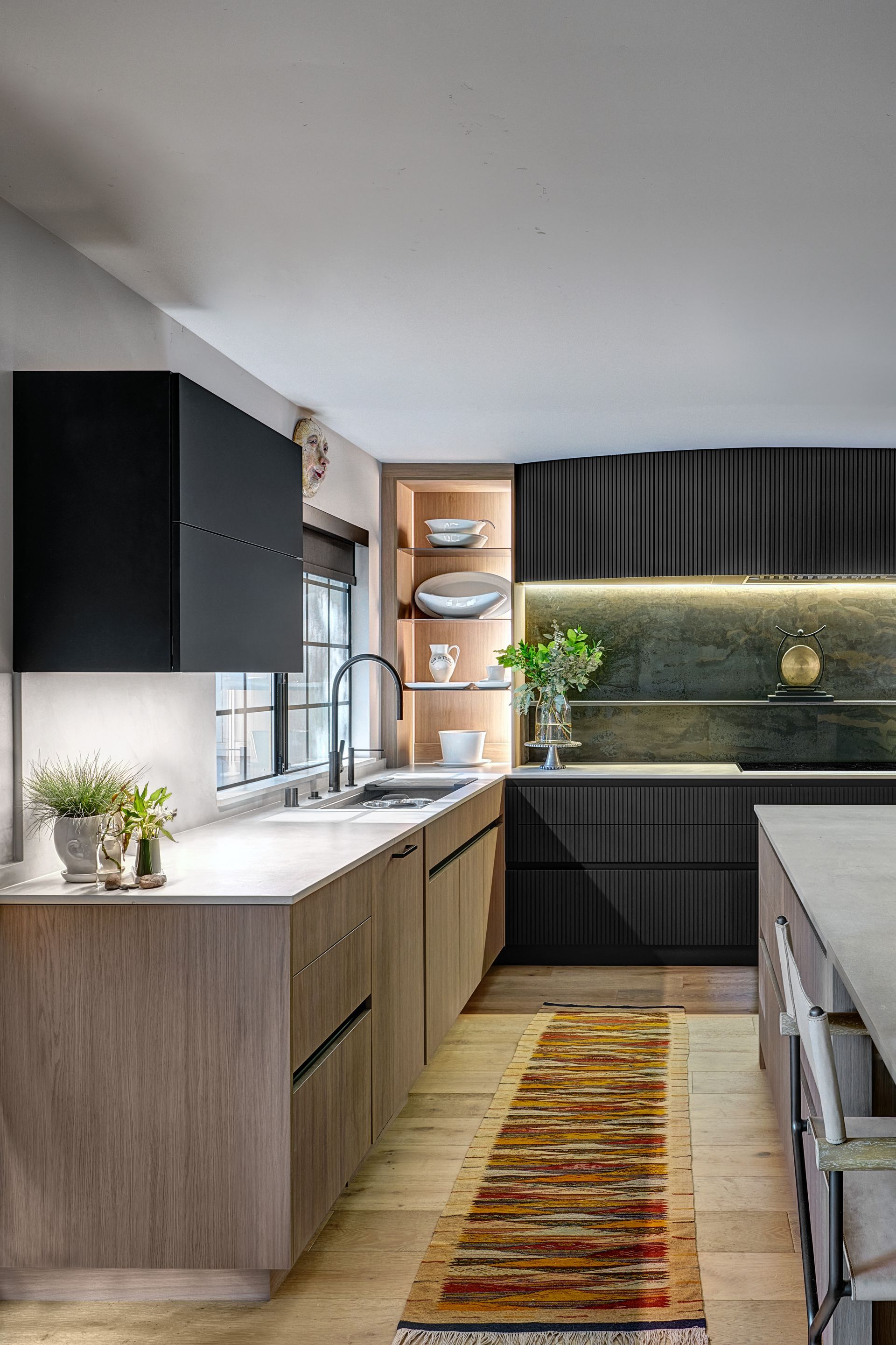Luxury kitchen remodel with dark cabinetry, light wood floors, and a dark accent wall above the sink.