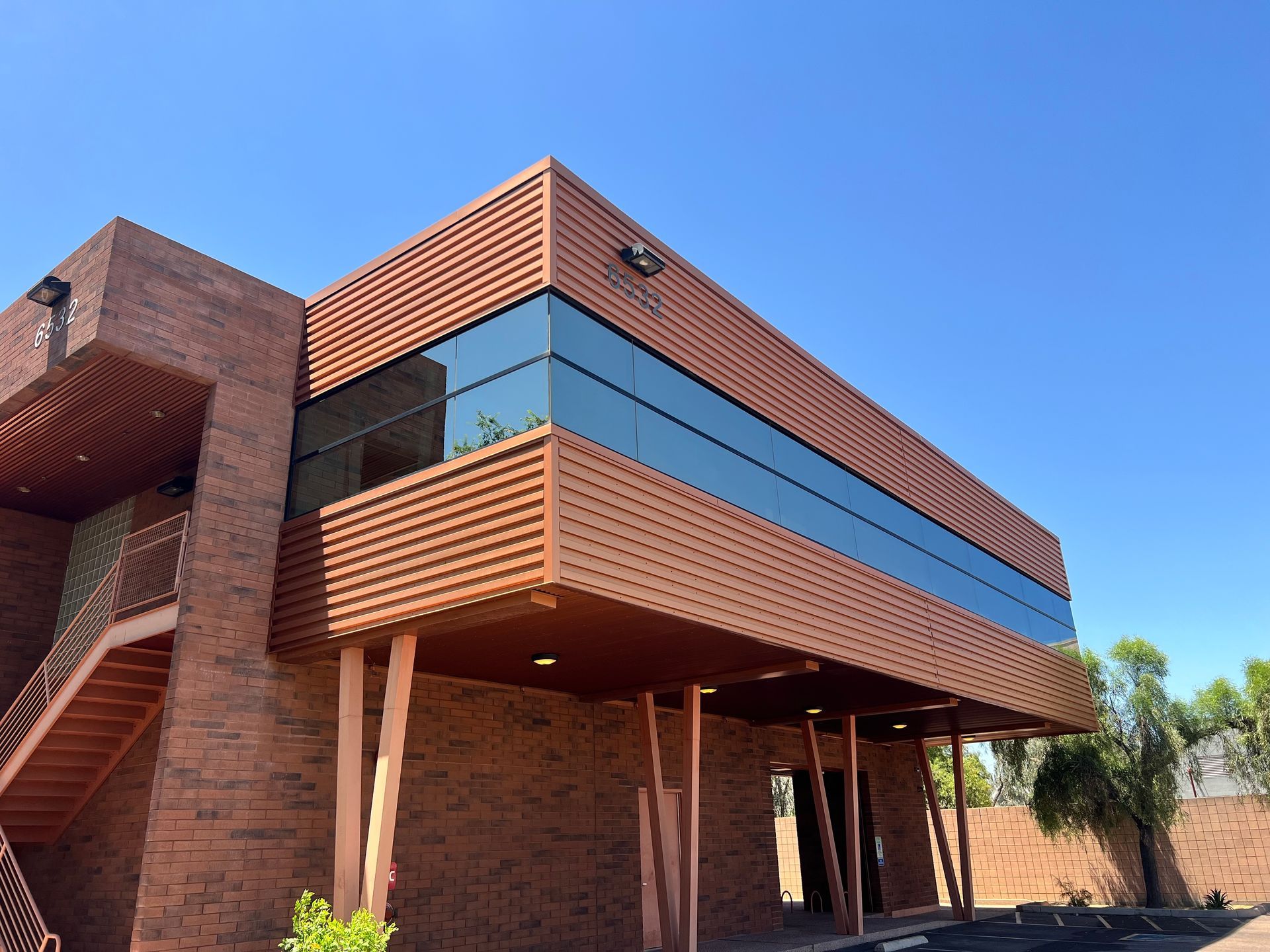 Modern brick building with wood slats, large blue windows, and a covered entrance under a clear sky