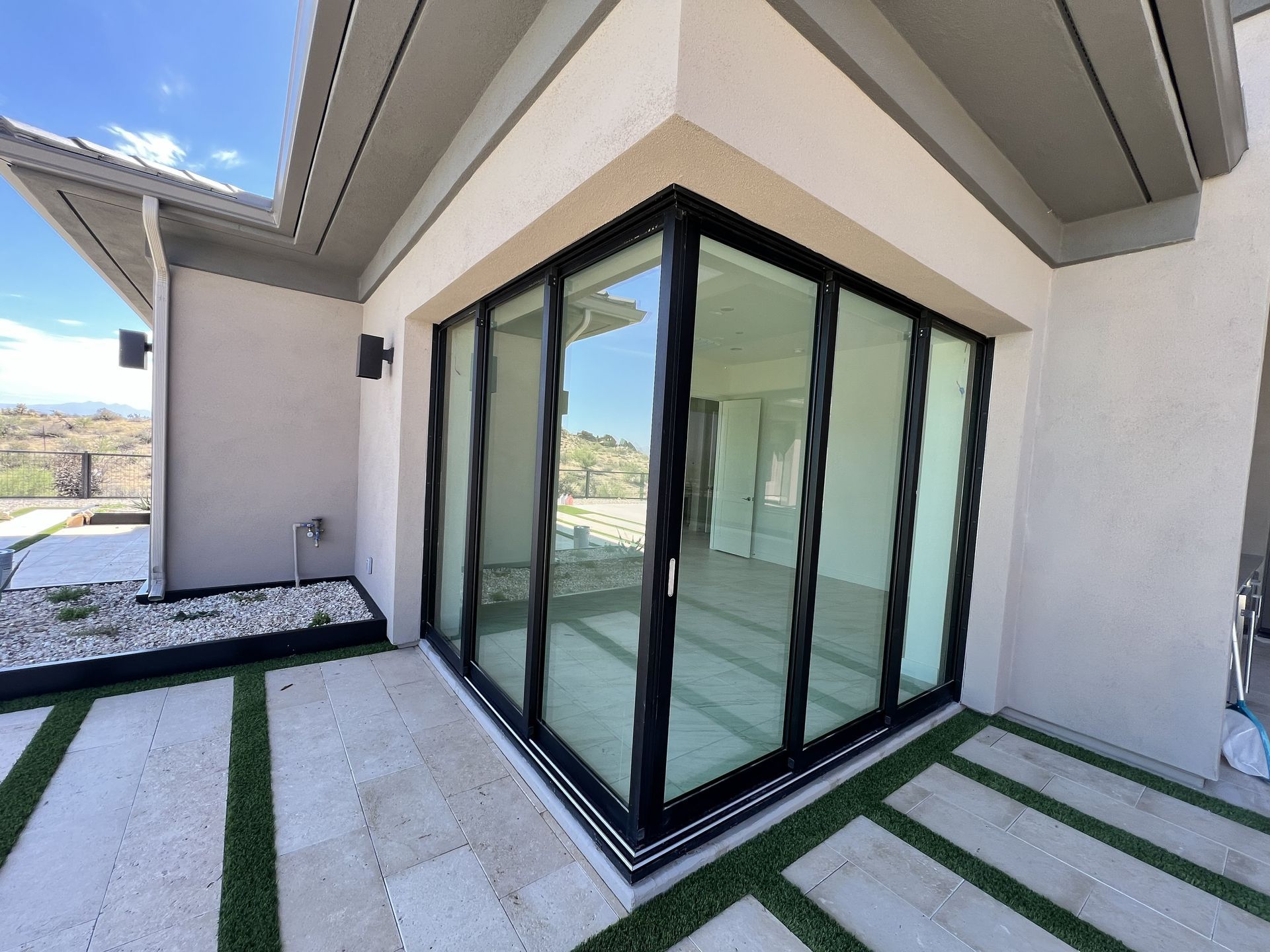 Modern house corner with black-framed glass doors, white walls, and a striped concrete patio