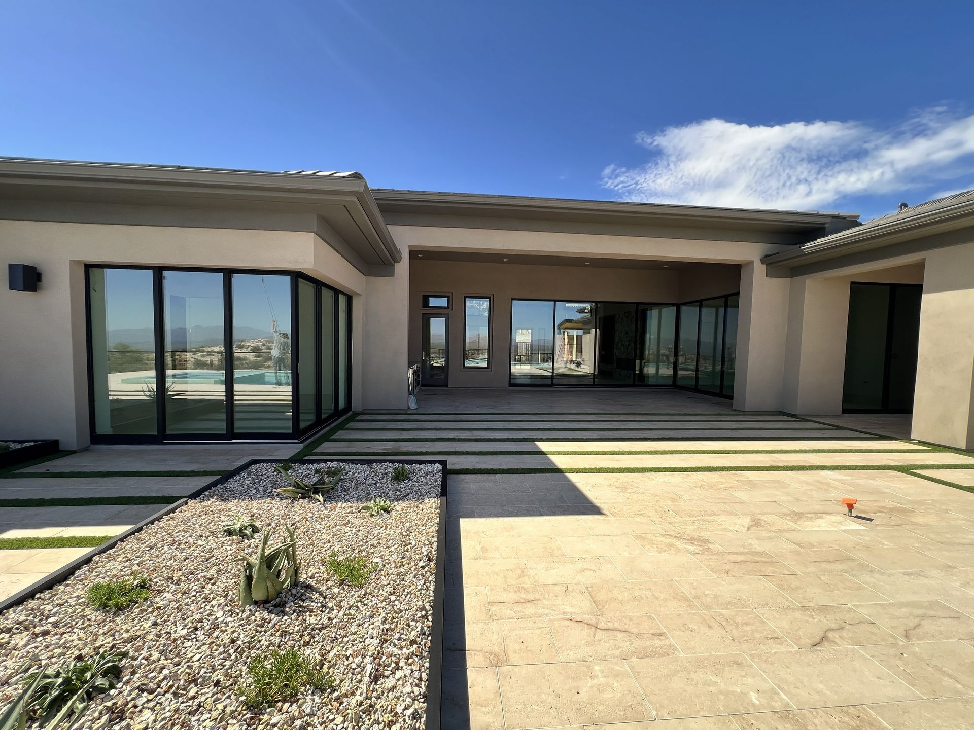 Modern house courtyard with large glass doors, beige walls, and a clear blue sky