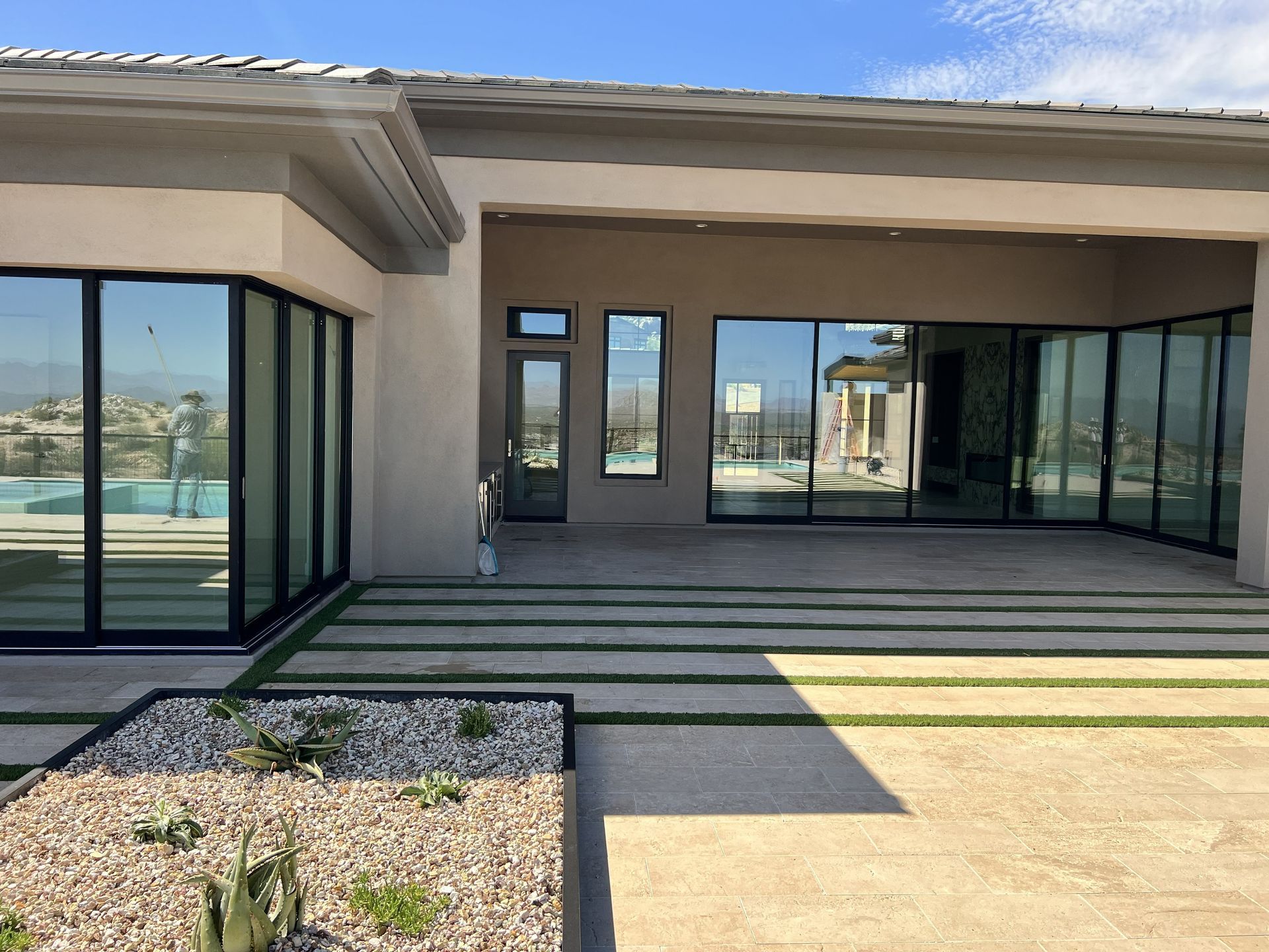 Modern house patio with sliding glass doors, stone pavers, and a small gravel planter under a clear sky