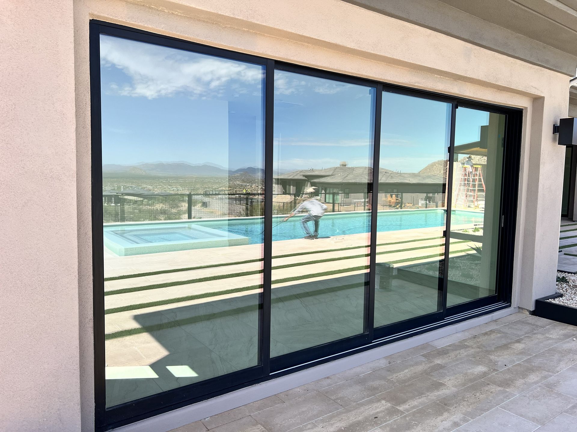 Patio sliding glass doors reflecting a pool deck and distant hills under a blue sky