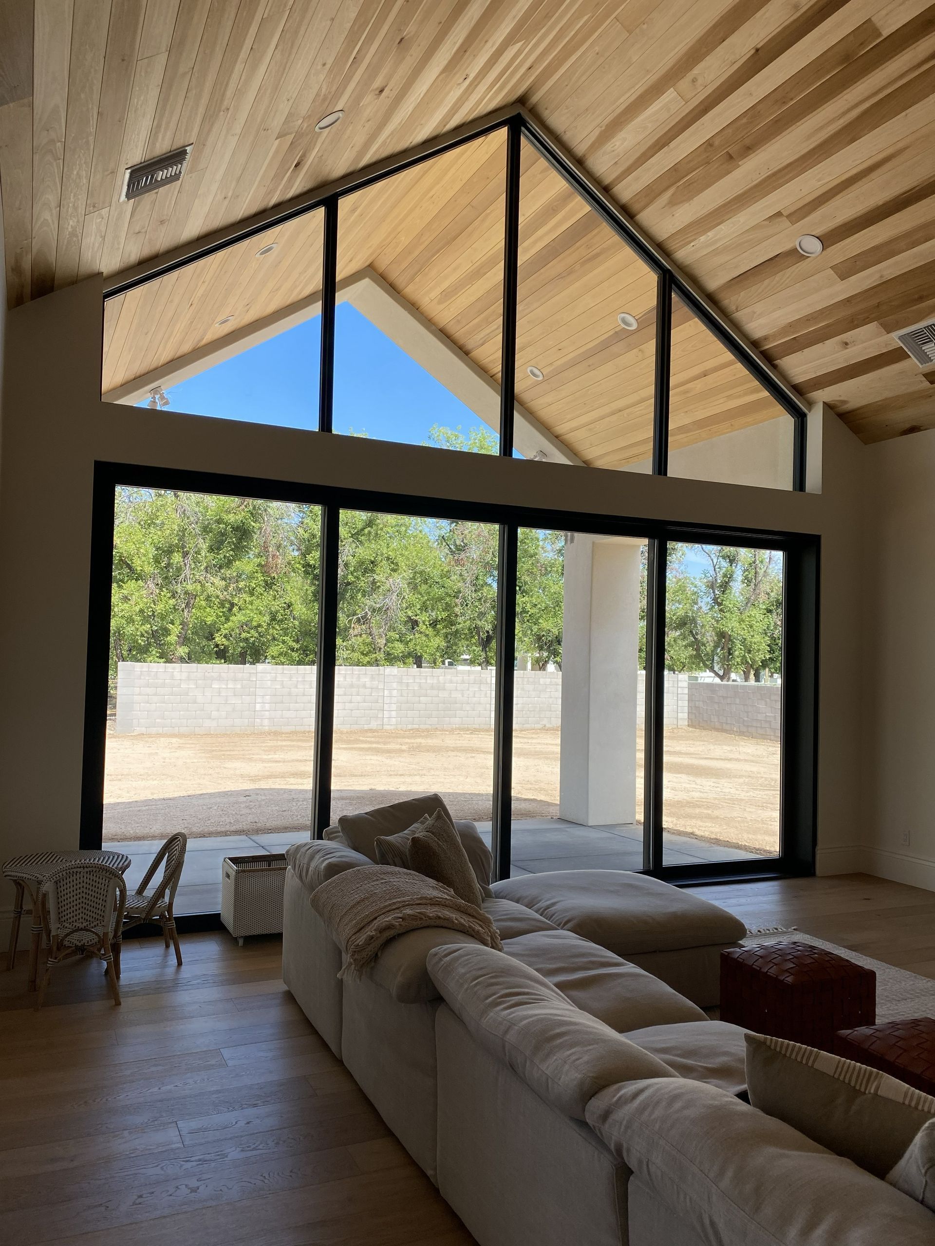 Modern living room with vaulted wood ceiling, large black-framed glass doors, and sectional sofa looking out to patio
