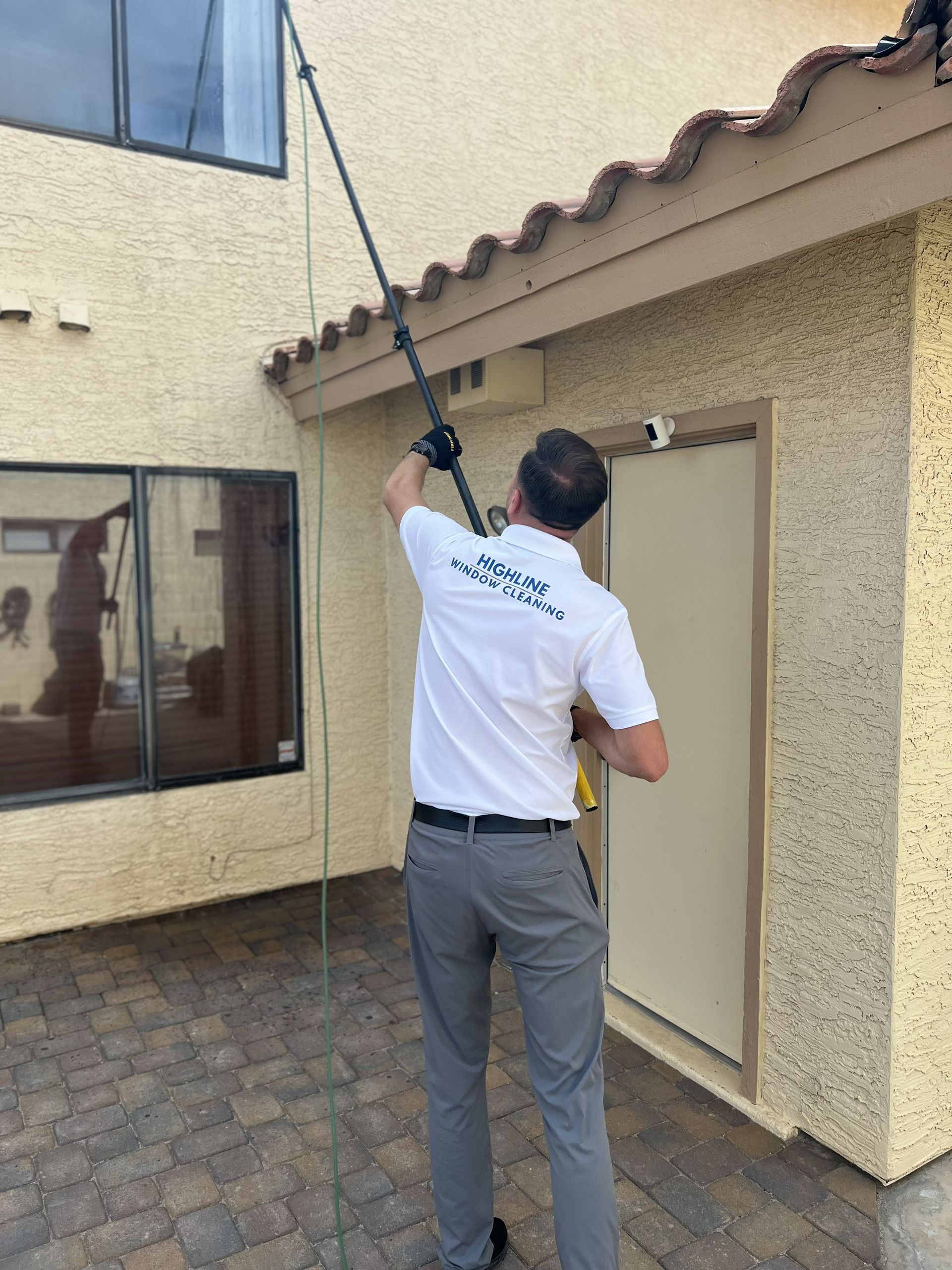 Worker using a long pole to clean gutters on a tan house exterior