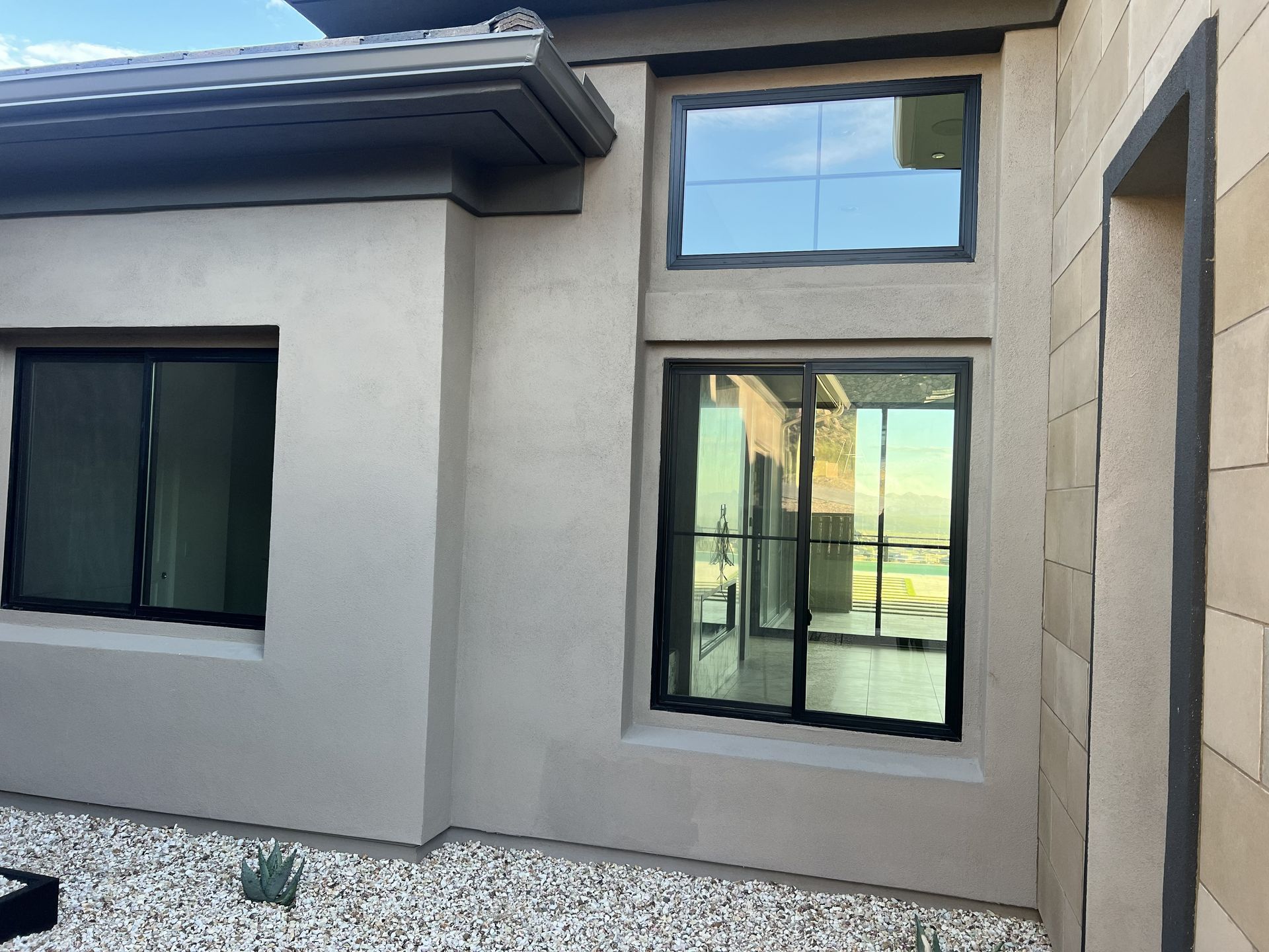 Modern stucco house exterior with black-framed windows and a gravel front yard