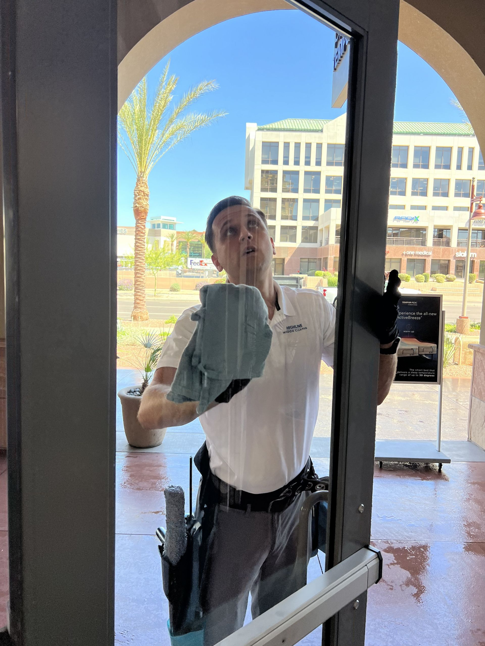 Person cleaning a glass door with a cloth, seen from inside a bright lobby.