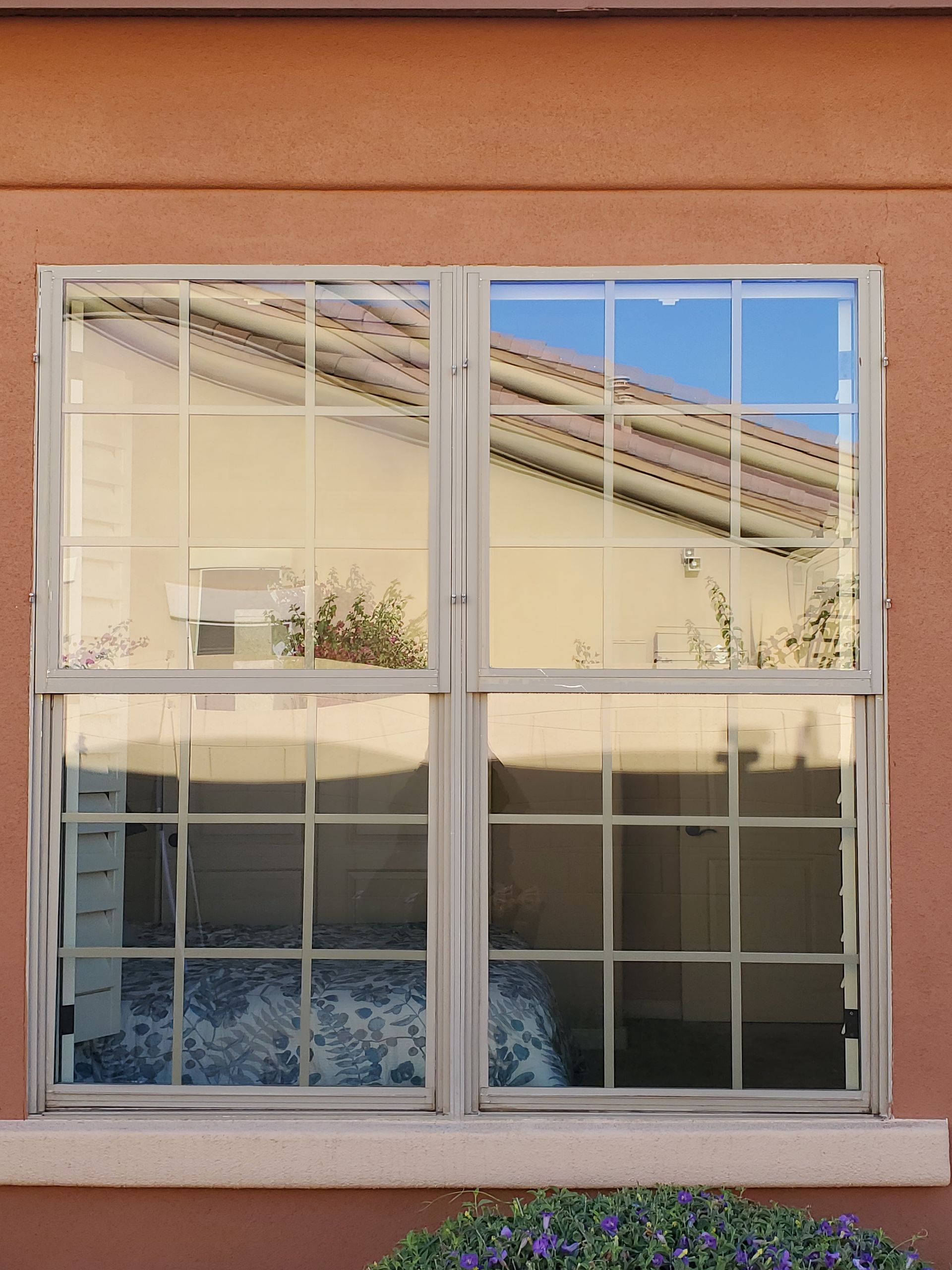 White-paned window reflecting a roof and sky on a peach stucco wall