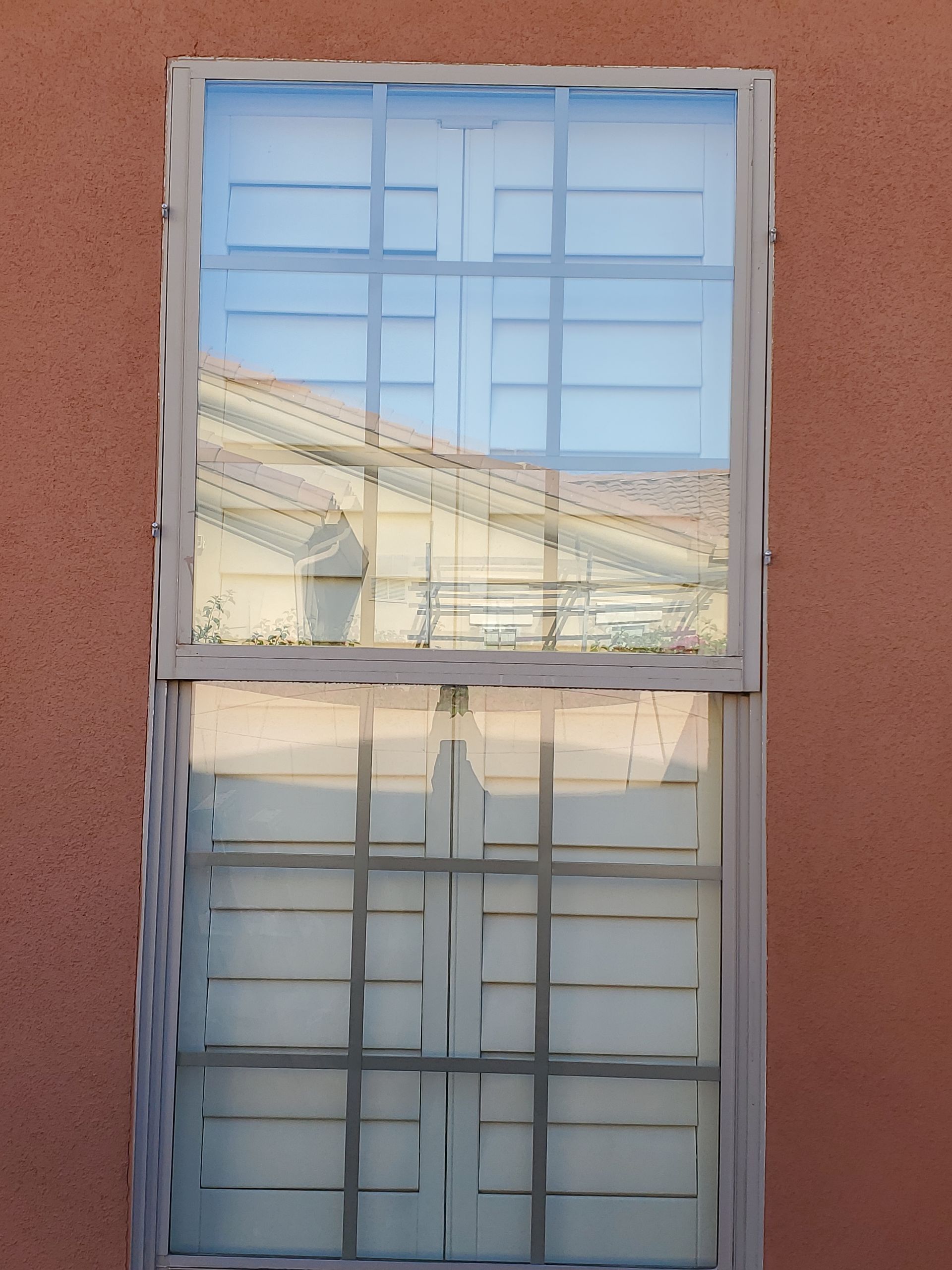 Two-pane window with white frames reflecting the sky on a peach-colored wall.