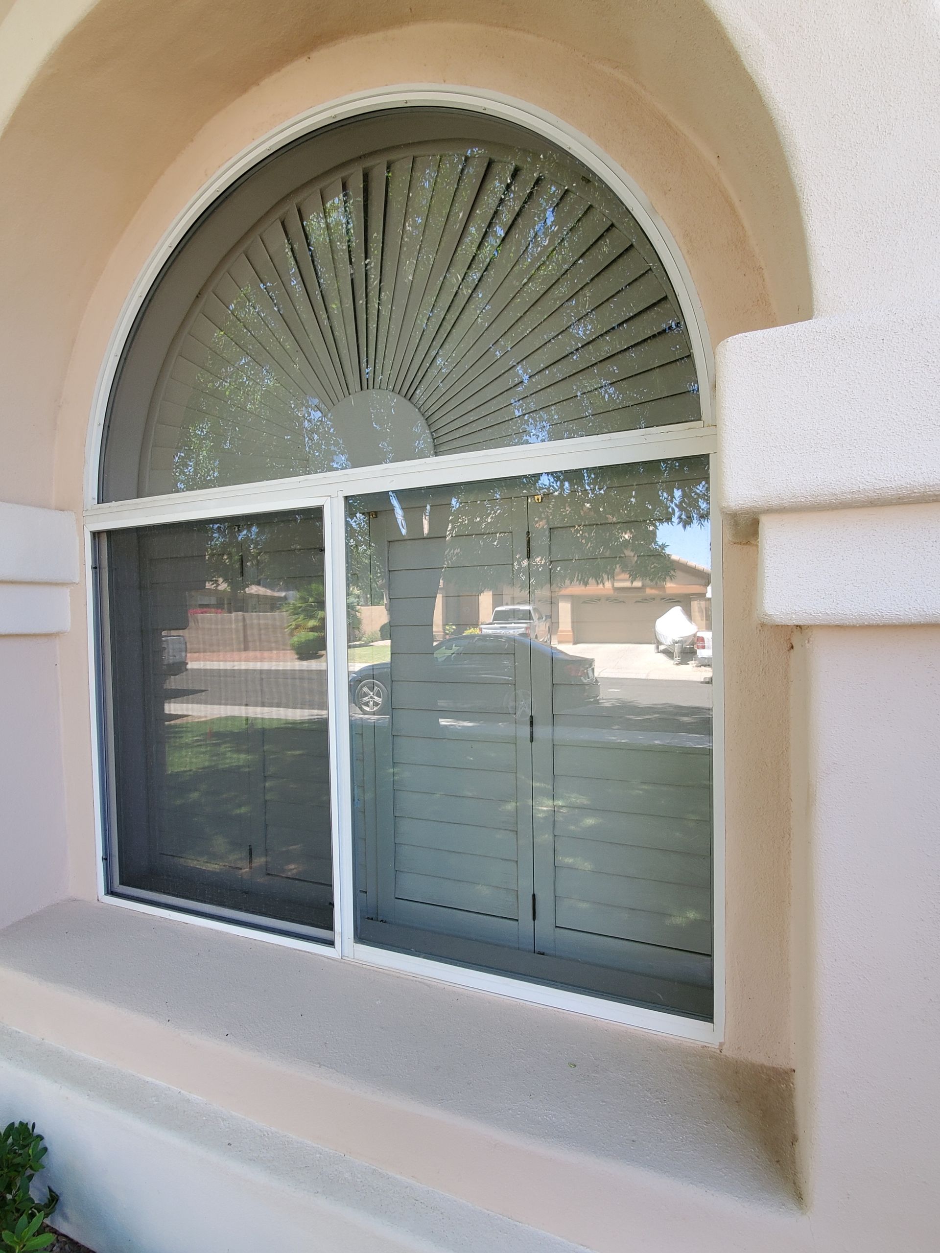 Arched window with white blinds on a beige stucco house exterior