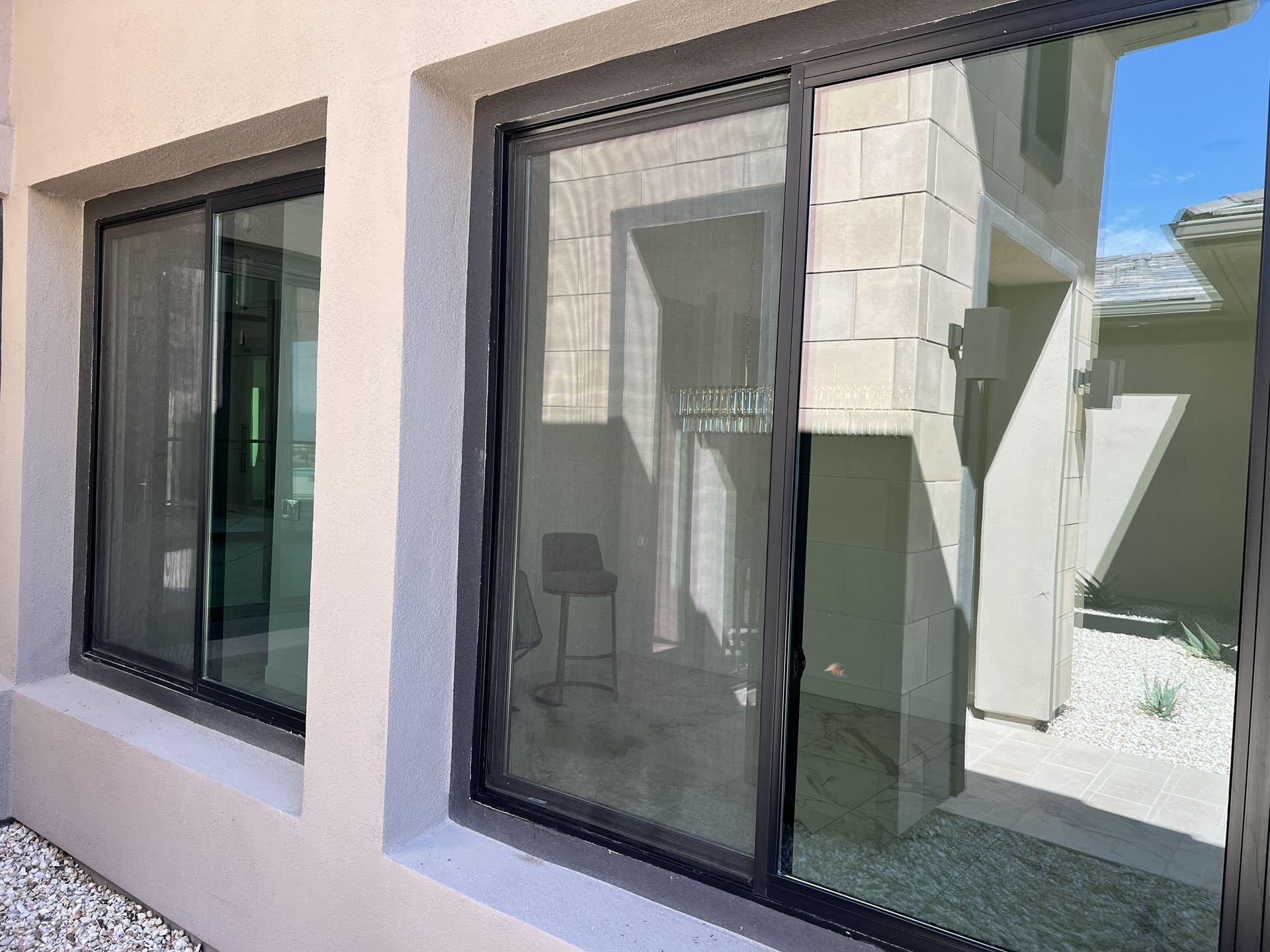 Modern house exterior with two dark-framed sliding glass windows reflecting a courtyard.