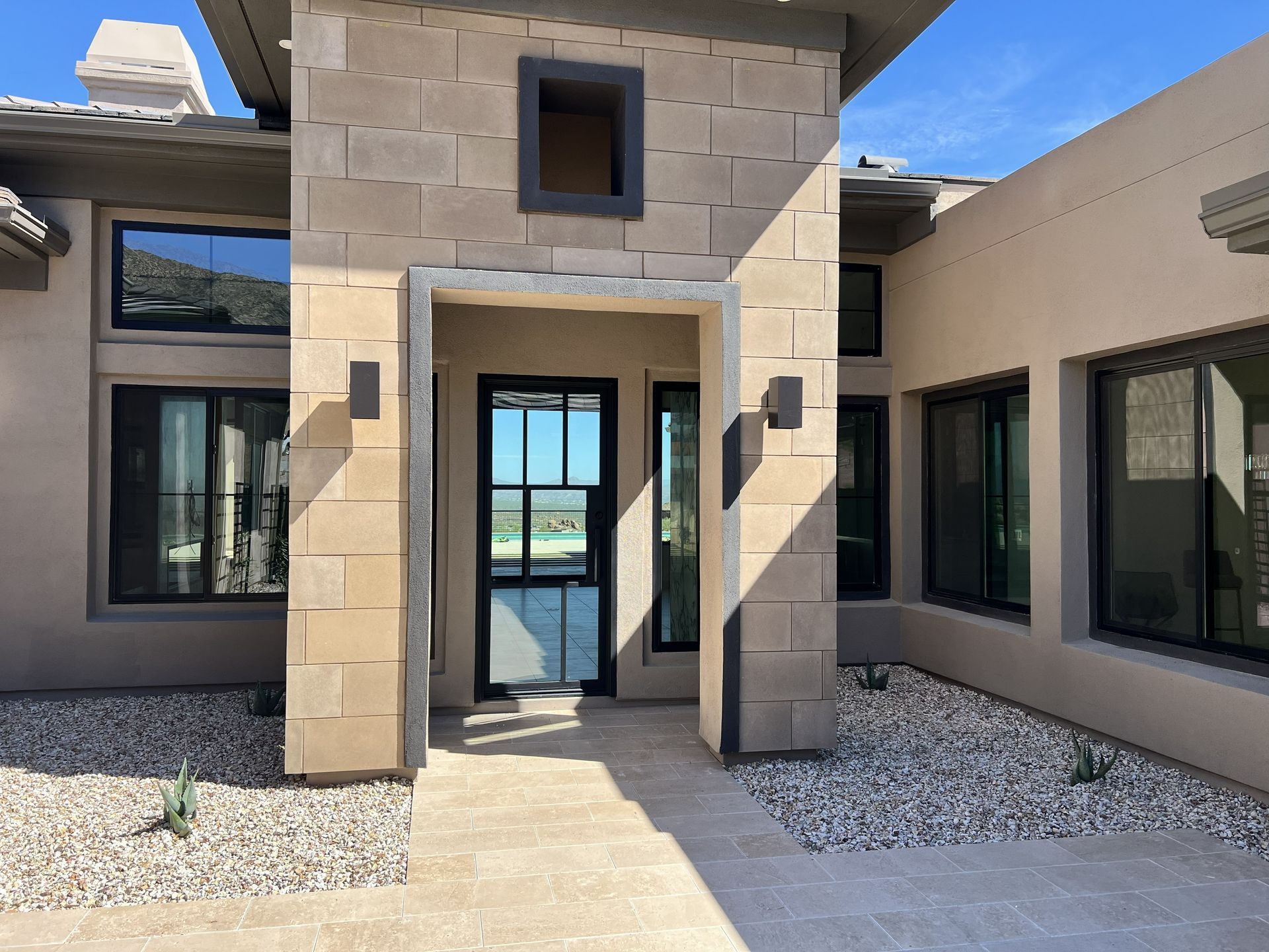 Desert-style building entrance with beige walls, dark-framed windows, and a glass door under a small entryway