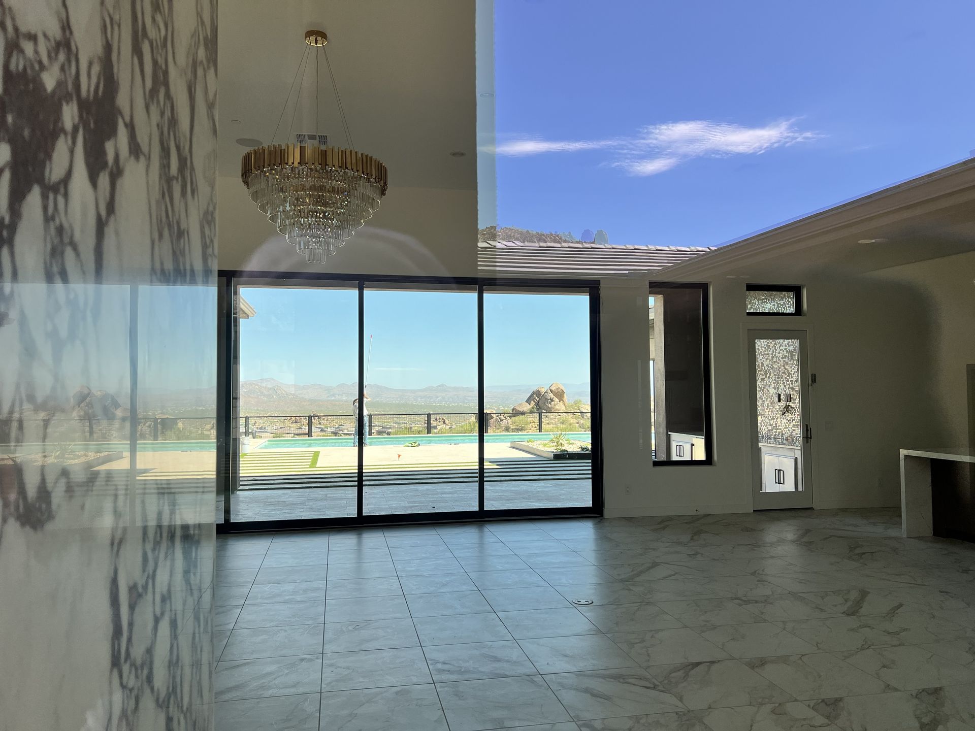 Modern empty living room with floor-to-ceiling glass doors and a chandelier overlooking a pool and mountains