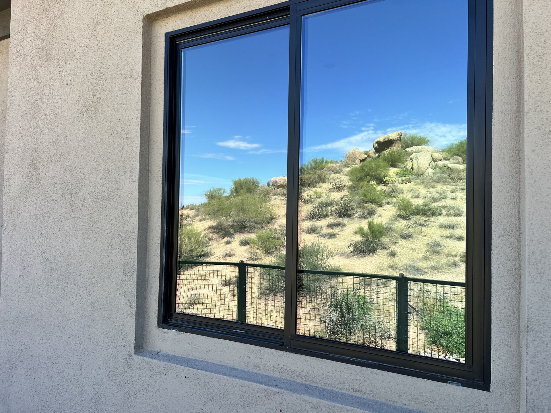 Window view of a sunny desert hillside with shrubs and a blue sky