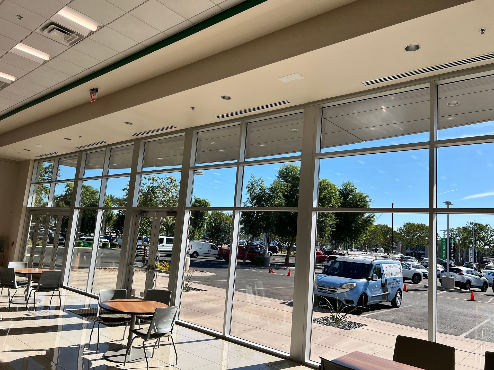 Empty café seating by large windows overlooking a sunny parking lot and trees