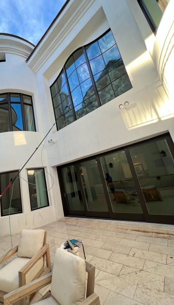 Modern white courtyard with large black-framed windows and beige patio furniture.