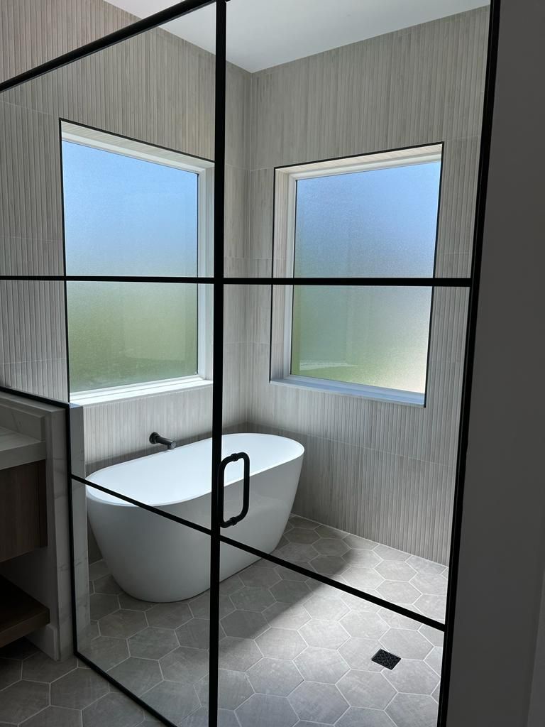 Modern bathroom with a freestanding tub, two windows, and a black-framed glass shower door