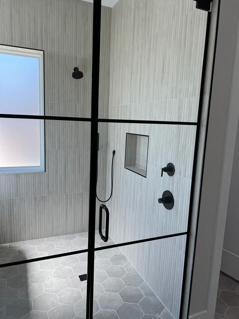 Black-framed glass shower door in a tiled bathroom with chrome handles and fixtures