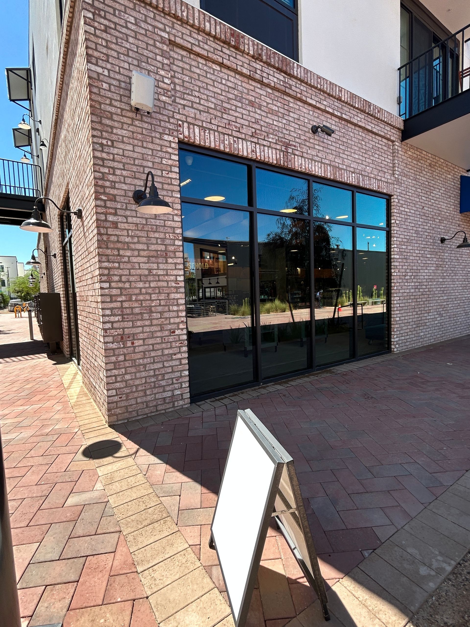 Brick storefront with large black-framed windows and a sandwich sign on a brick-paved walkway