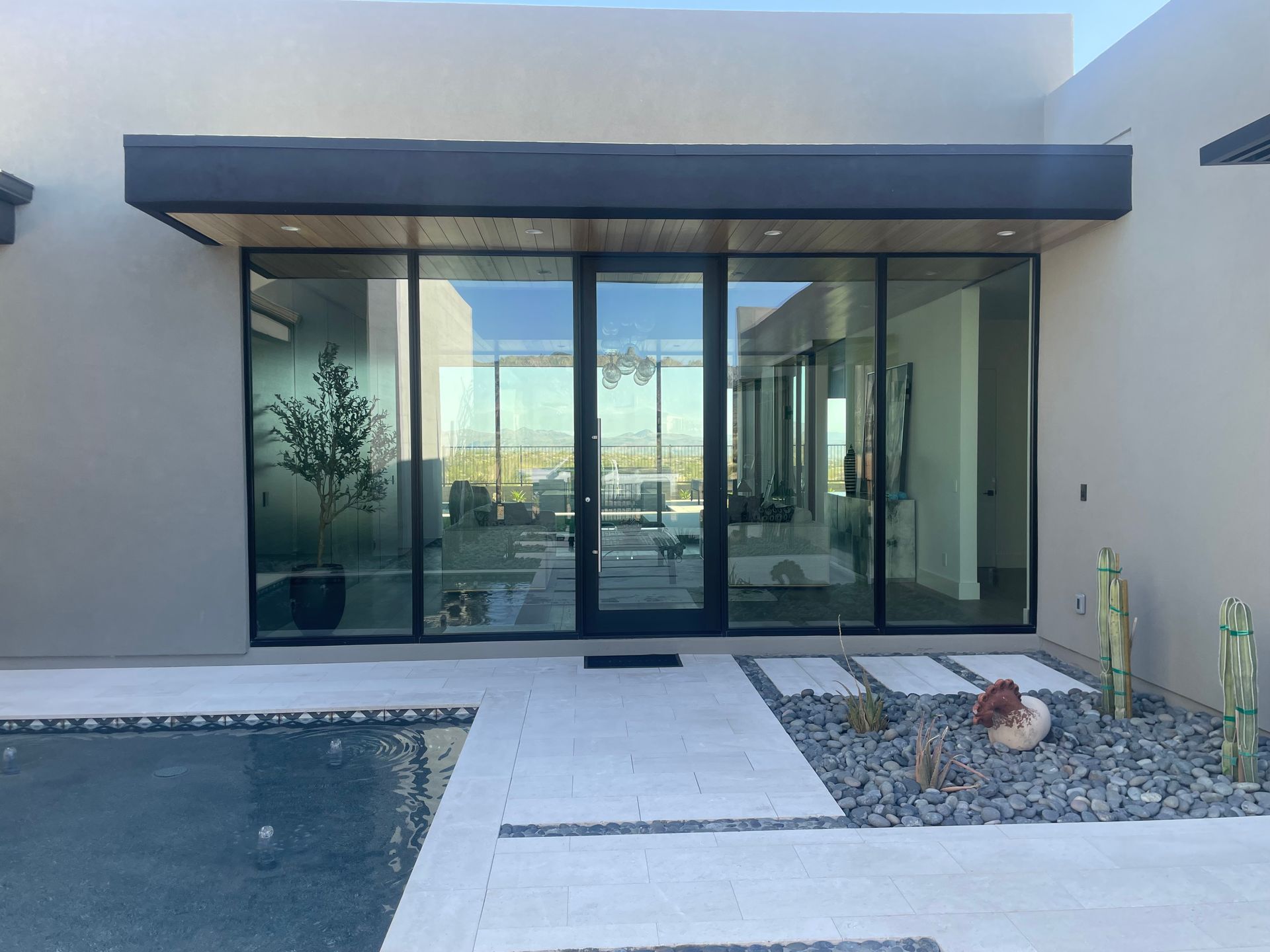 Modern home entrance with large glass sliding doors, a dark awning, and a front walkway beside a small pool.