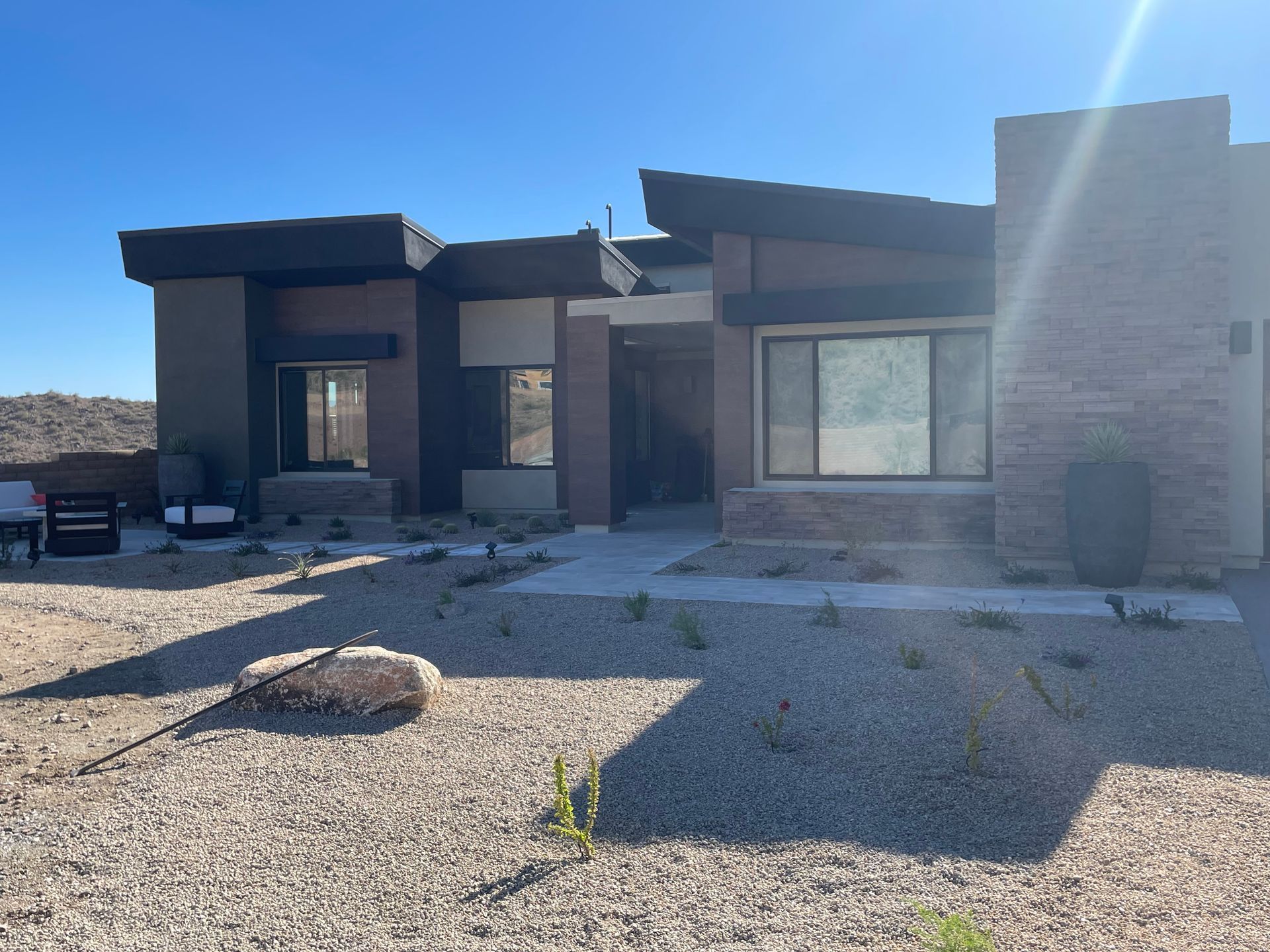 Sunlit desert-style house with stone facade, gravel yard, and a parked vehicle on the left
