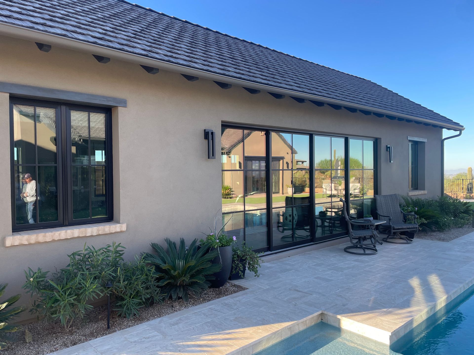 Modern stucco house exterior with large glass doors, windows, and a paved patio in front