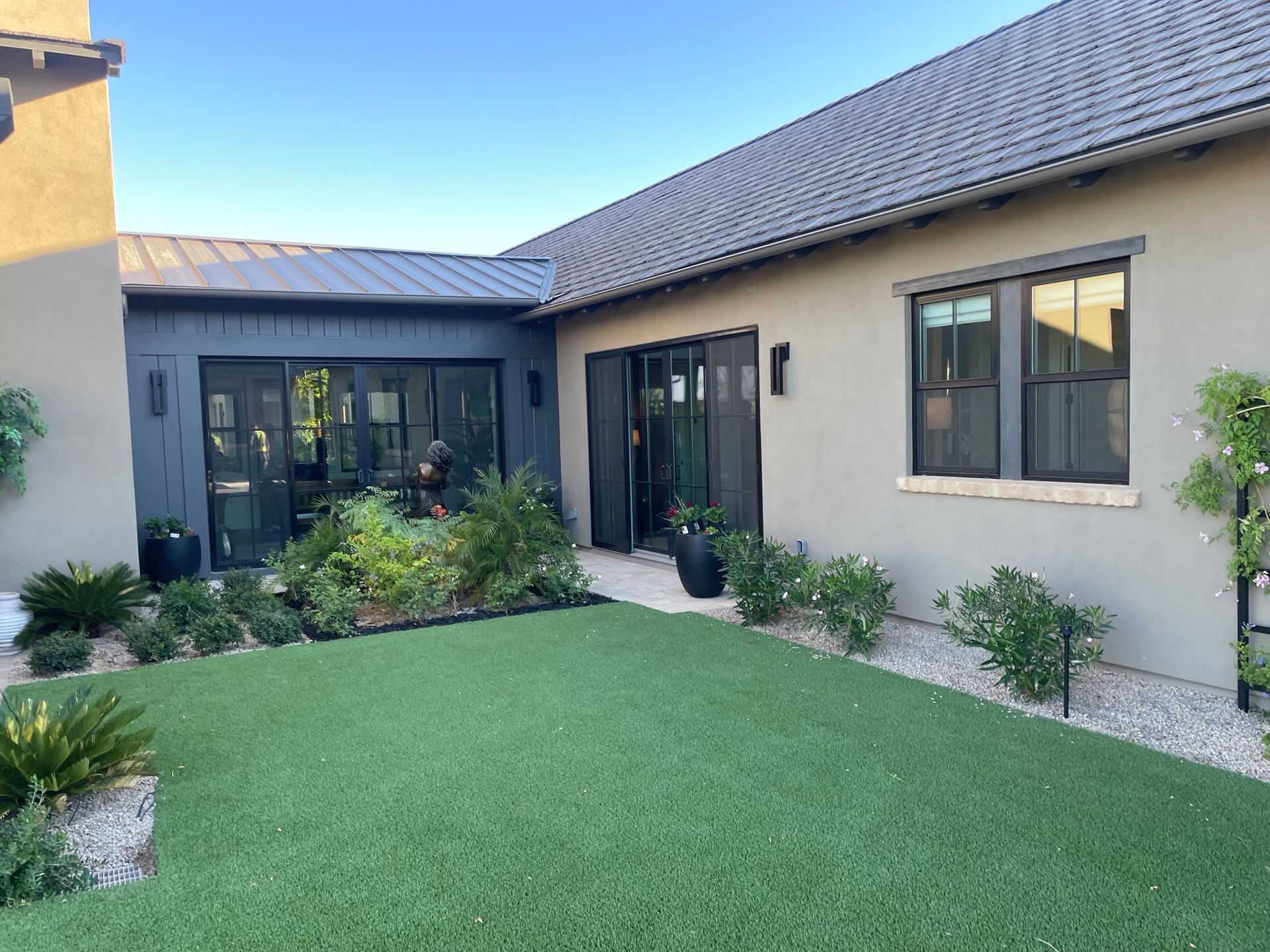 Modern home courtyard with green lawn, beige stucco walls, and black-framed windows and doors