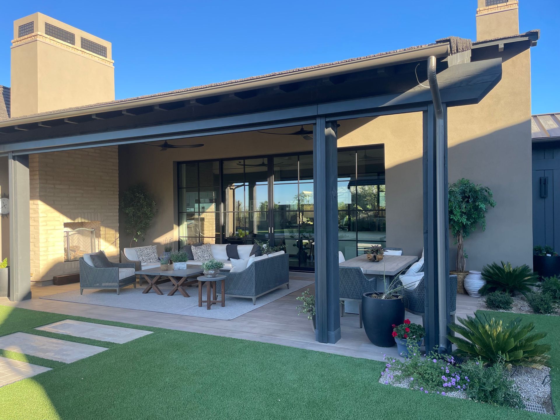 Patio with covered seating, glass doors, and a grassy yard beside a stucco house.