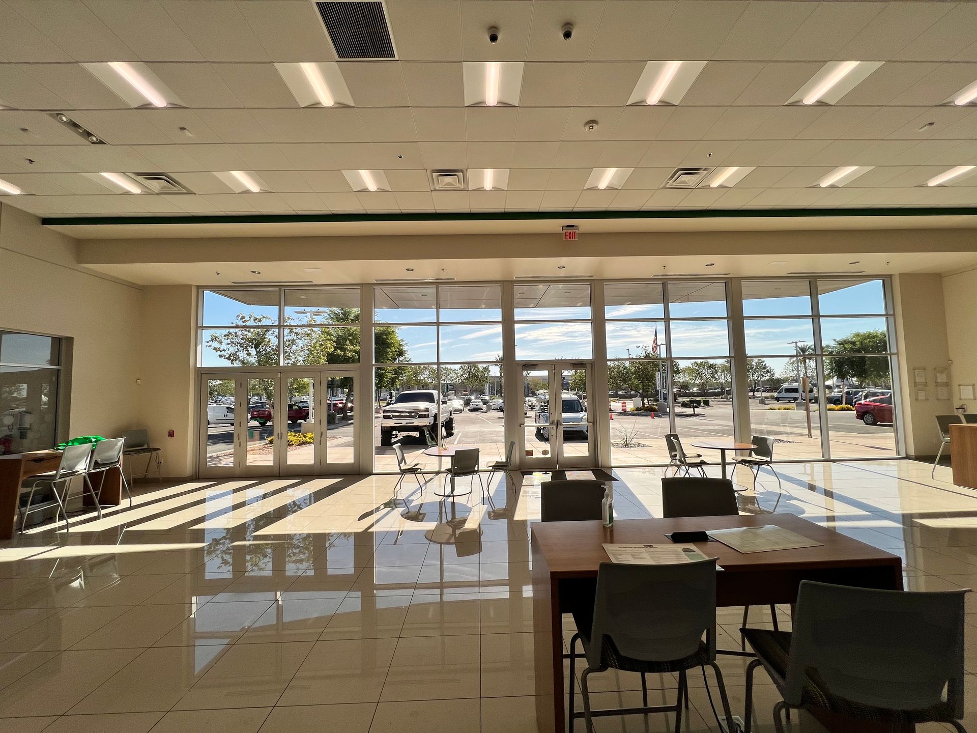 Empty lobby with glossy tile floor, tables and chairs, and large front windows overlooking a parking lot